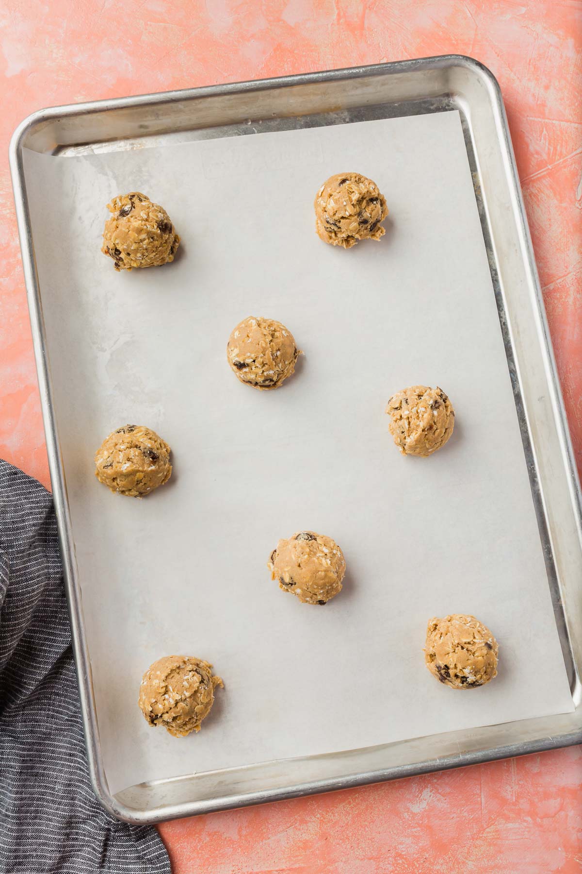 Gluten-free oatmeal raisin cookie dough balls spaced out on a parchment lined baking sheet before going in the oven.