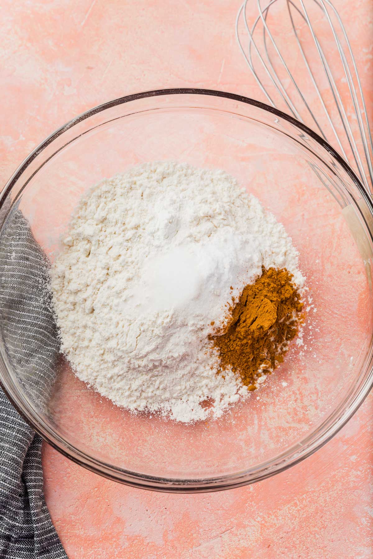 A glass mixing bowl with gluten-free flour, cinnamon, salt, baking soda and baking powder in it before mixing together.