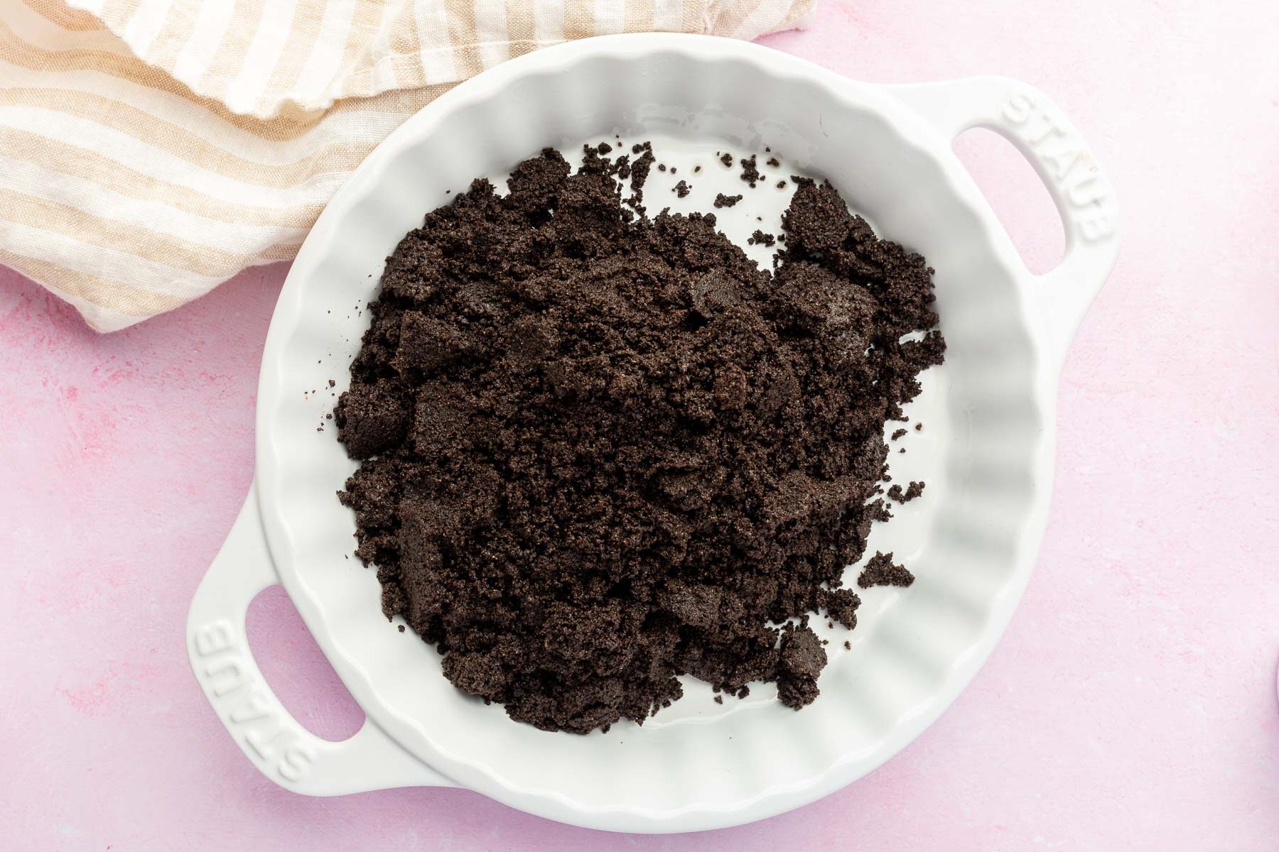 A mound of gluten-free Oreo crumbles in a white tart pan before pressing into an even layer.