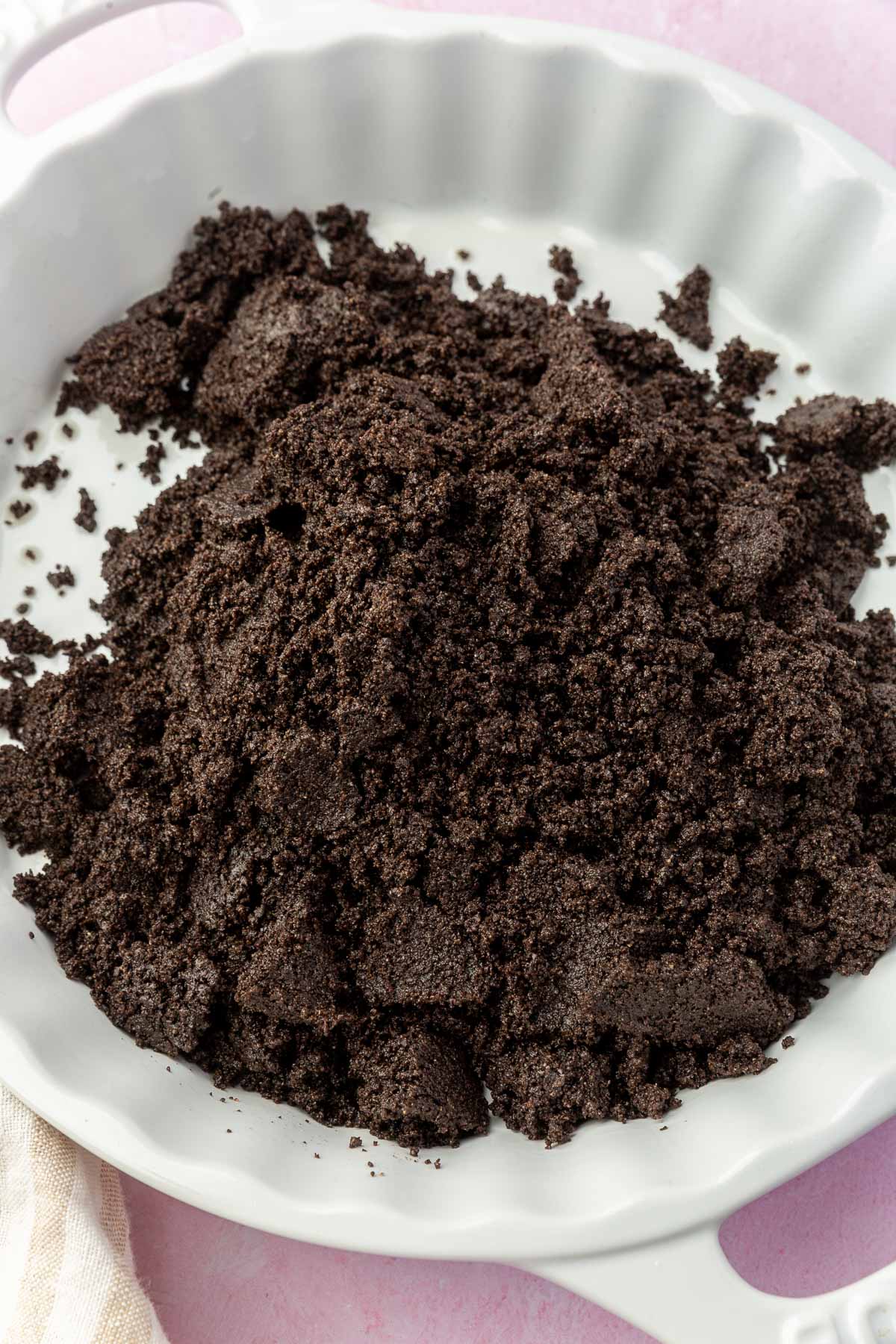 A mound of gluten-free Oreo crumbles in a white tart pan before pressing into an even layer.