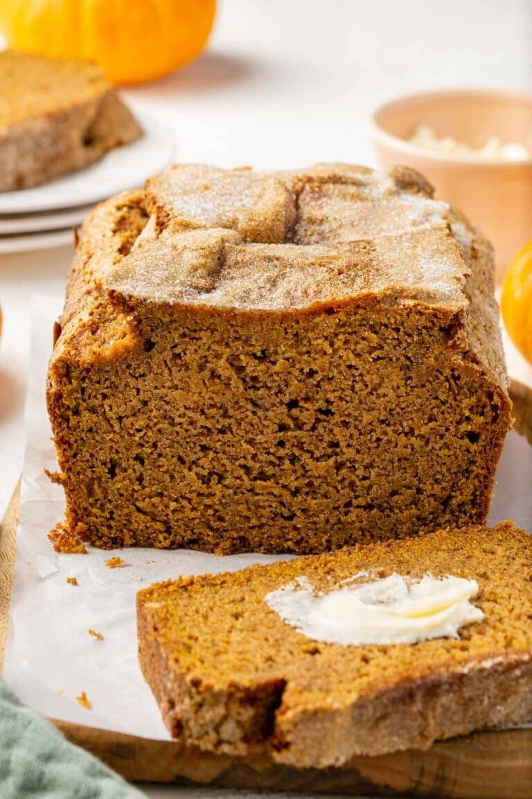 A partially cut loaf of gluten free pumpkin bread on a board.