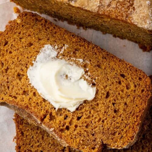 A close up of two slices of gluten free pumpkin bread sliced off from the larger loaf and slathered with butter.