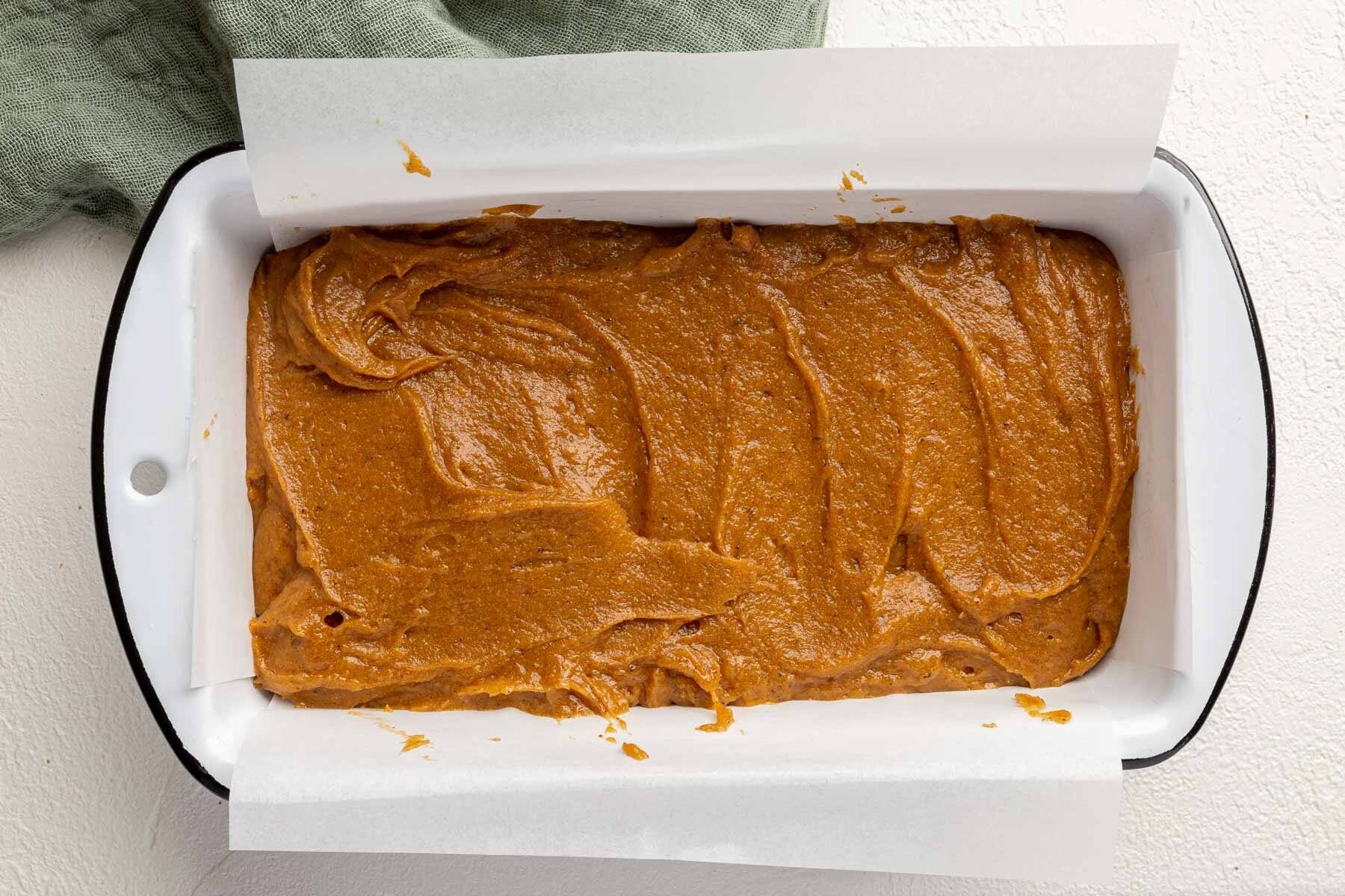 A parchment lined loaf pan filled with gluten-free pumpkin bread batter before baking in the oven.