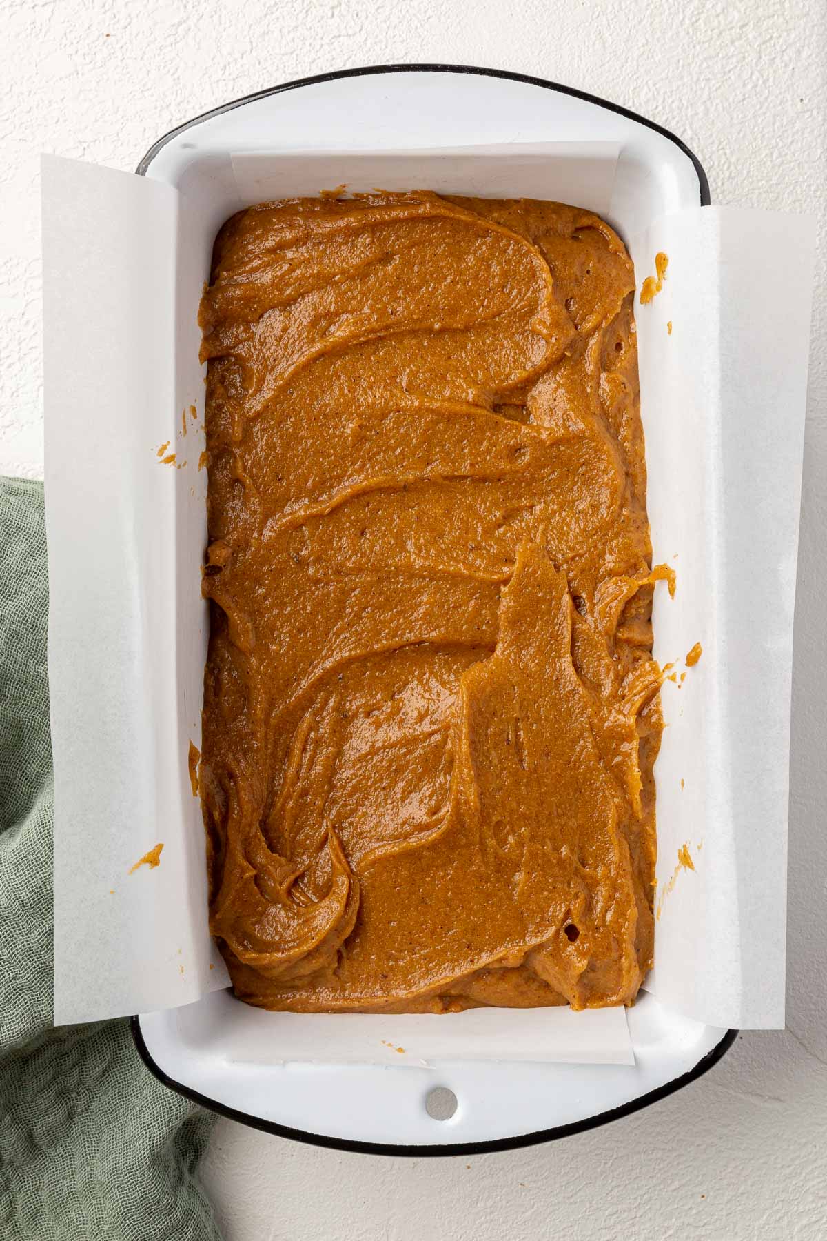 A parchment lined loaf pan filled with gluten-free pumpkin bread batter before baking in the oven.