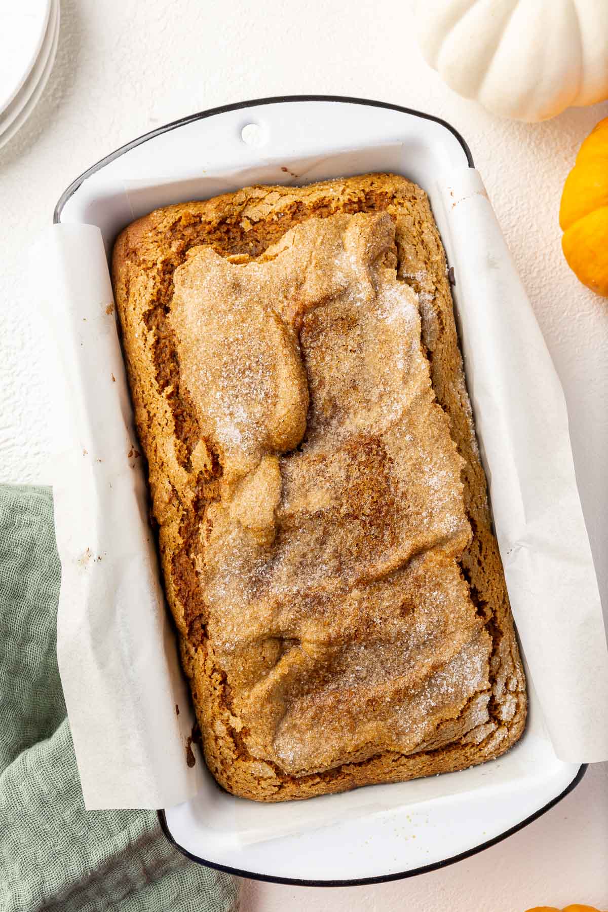 A loaf of gluten-free pumpkin bread in a white loaf pan with mini pumpkins to the side.