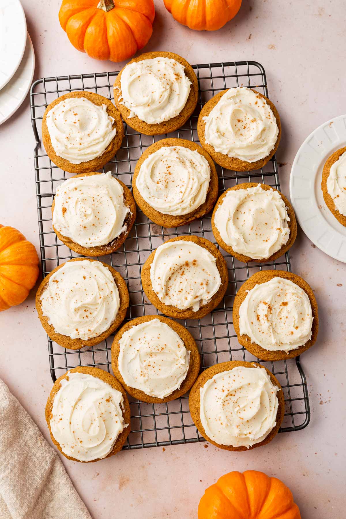 An overhead view of gluten-free pumpkin cookies topped with cream cheese frosting on a wire cooling rack with mini pumpkins surrounding the cookies.