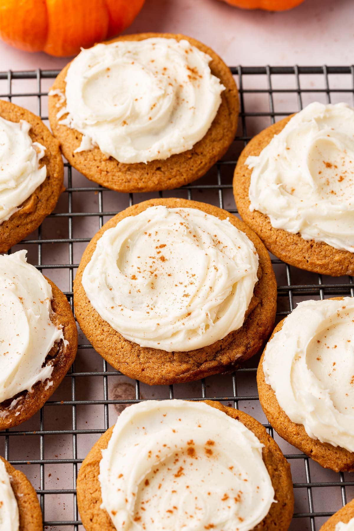 Gluten free pumpkin cookies topped with cream cheese frosting on a wire cooling rack.