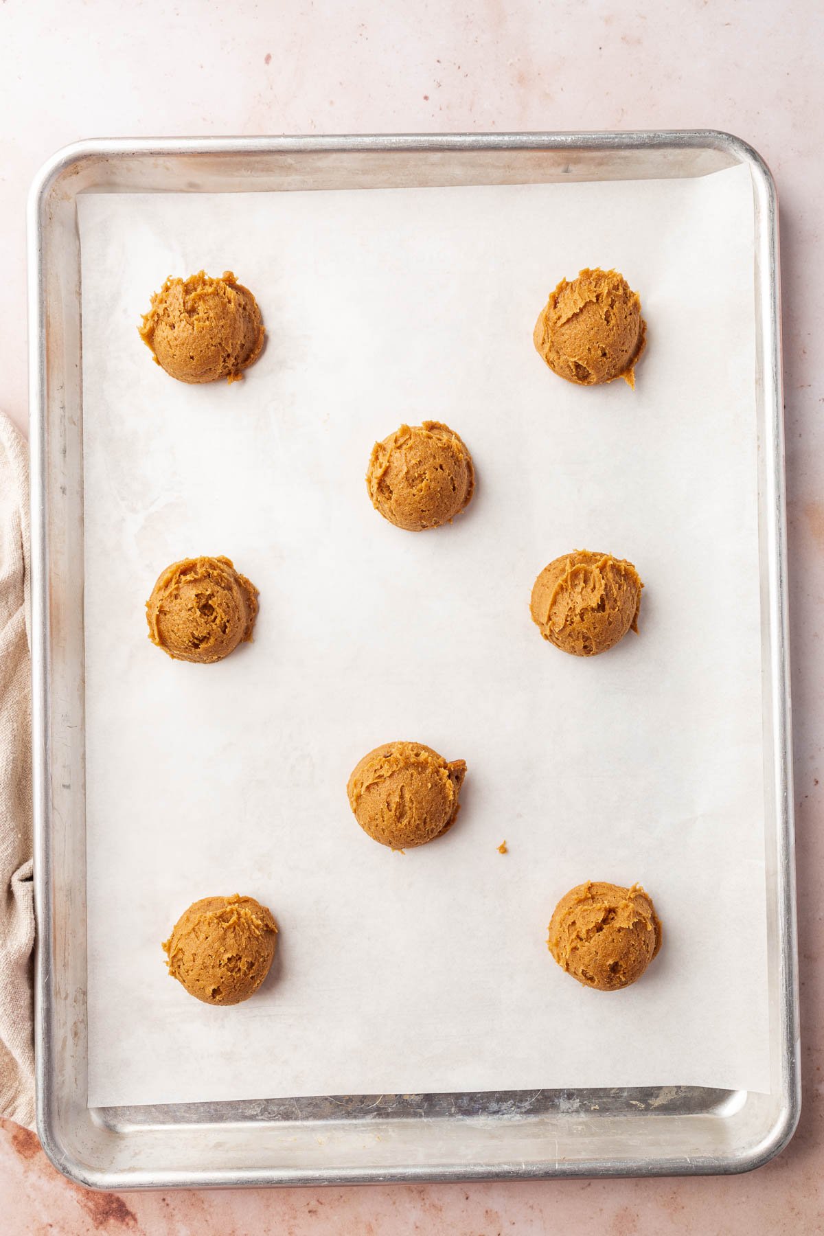 A baking sheet lined with parchment paper and topped with eight gluten-free pumpkin cookie dough balls before baking in the oven.