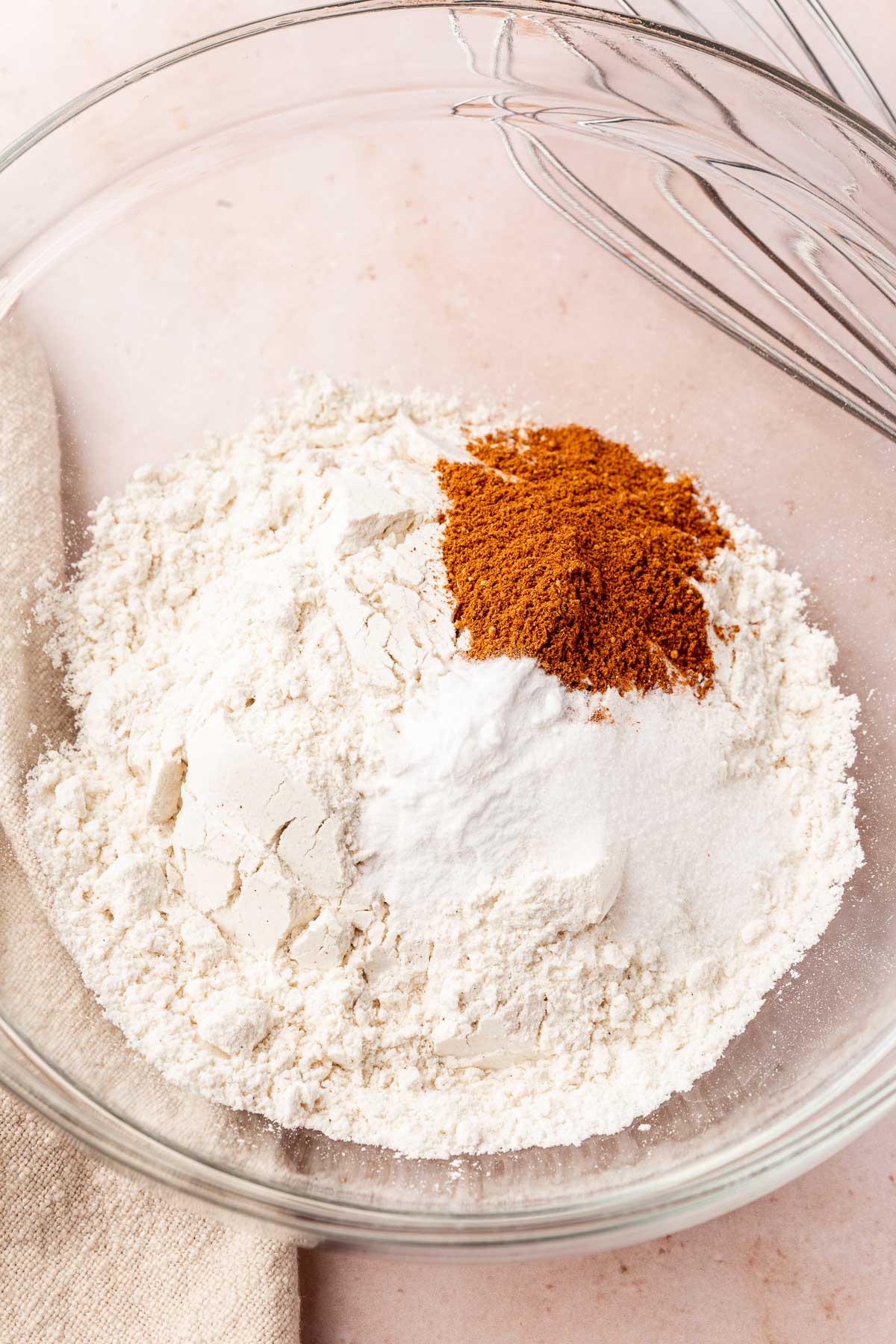 A glass mixing bowl with gluten-free flour, baking soda, baking powder, salt and pumpkin pie spice before whisking together.