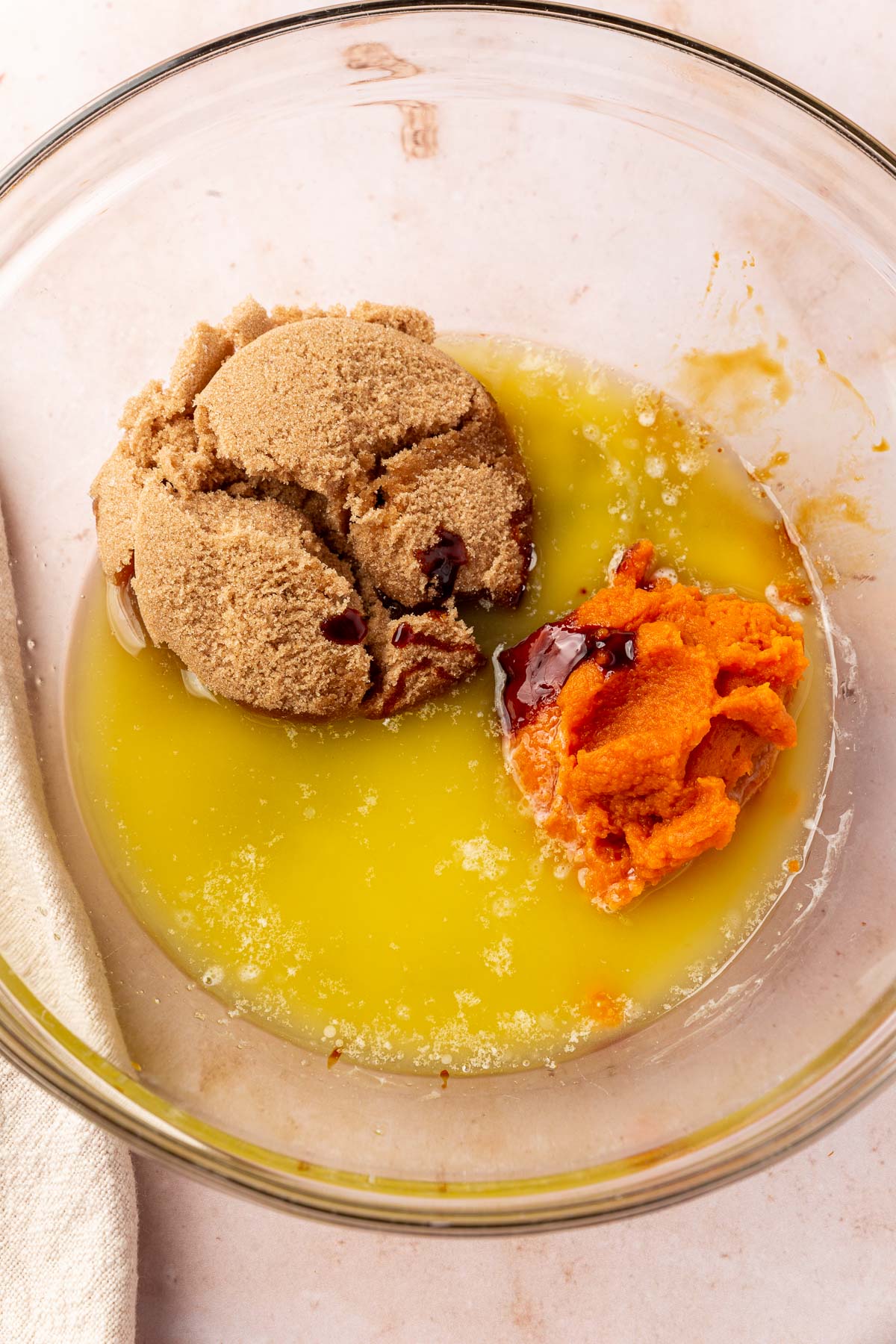 A glass mixing bowl with brown sugar, melted butter, pumpkin puree, and molasses before mixing together.