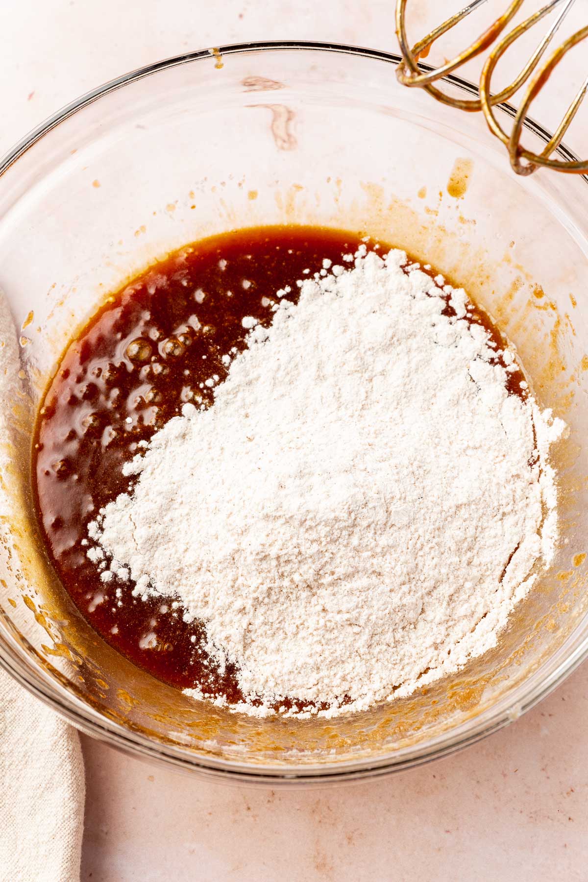 A glass mixing bowl with dry ingredients on top of a brown sugar, pumpkin, melted butter mixture.