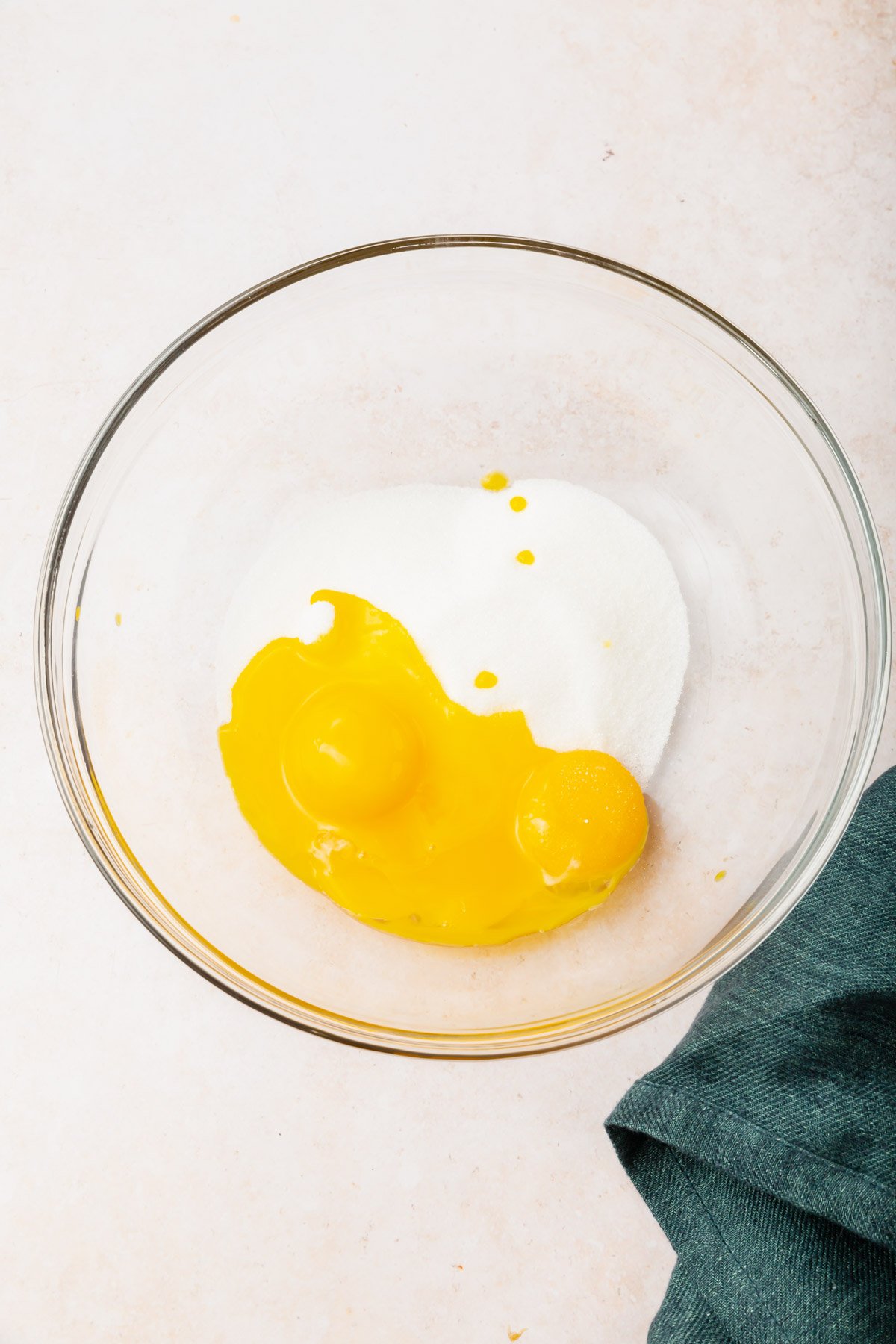A glass mixing bowl with two egg yolks and granulated sugar in it before mixing together.