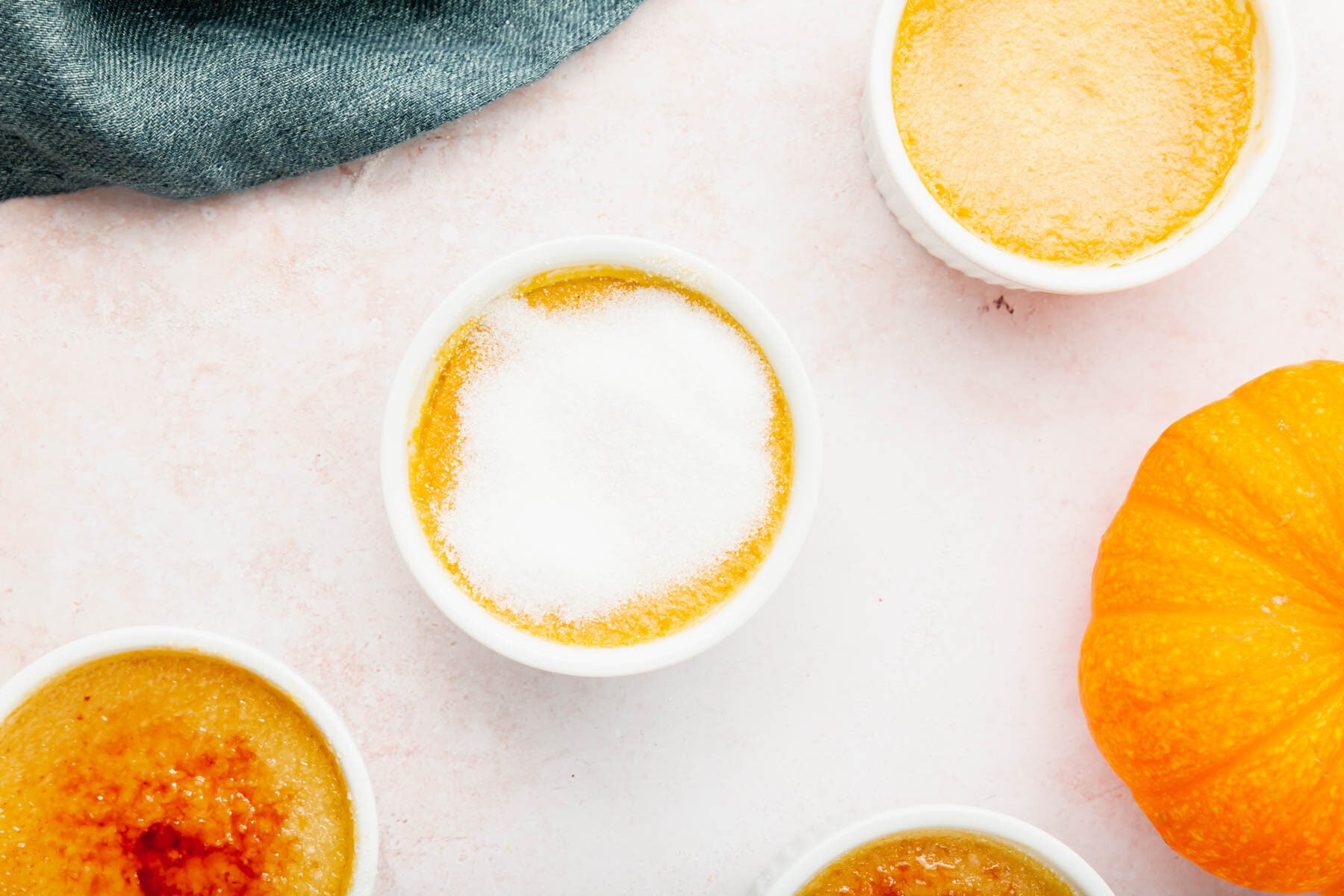 Ramekins of pumpkin crème brûlée with raw granulated sugar on them before torching.