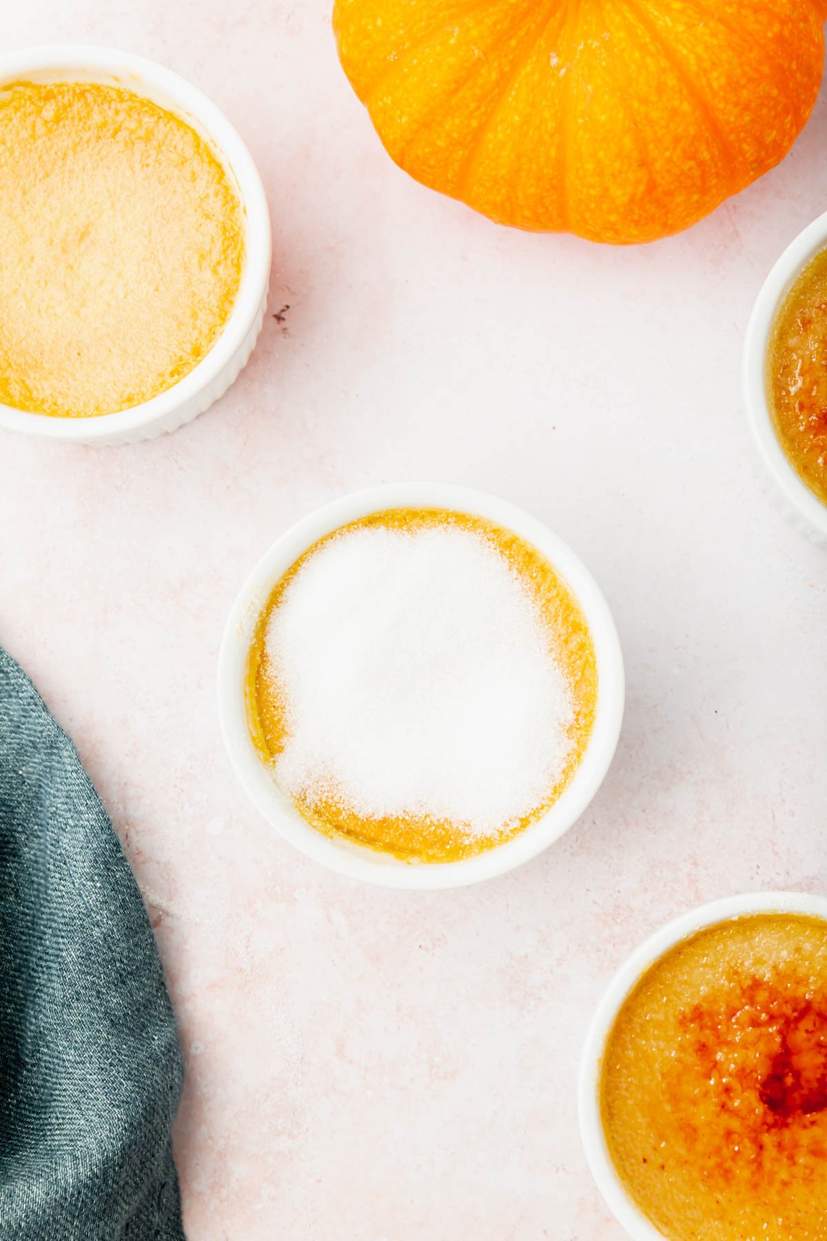 Ramekins of pumpkin crème brûlée with raw granulated sugar on them before torching.