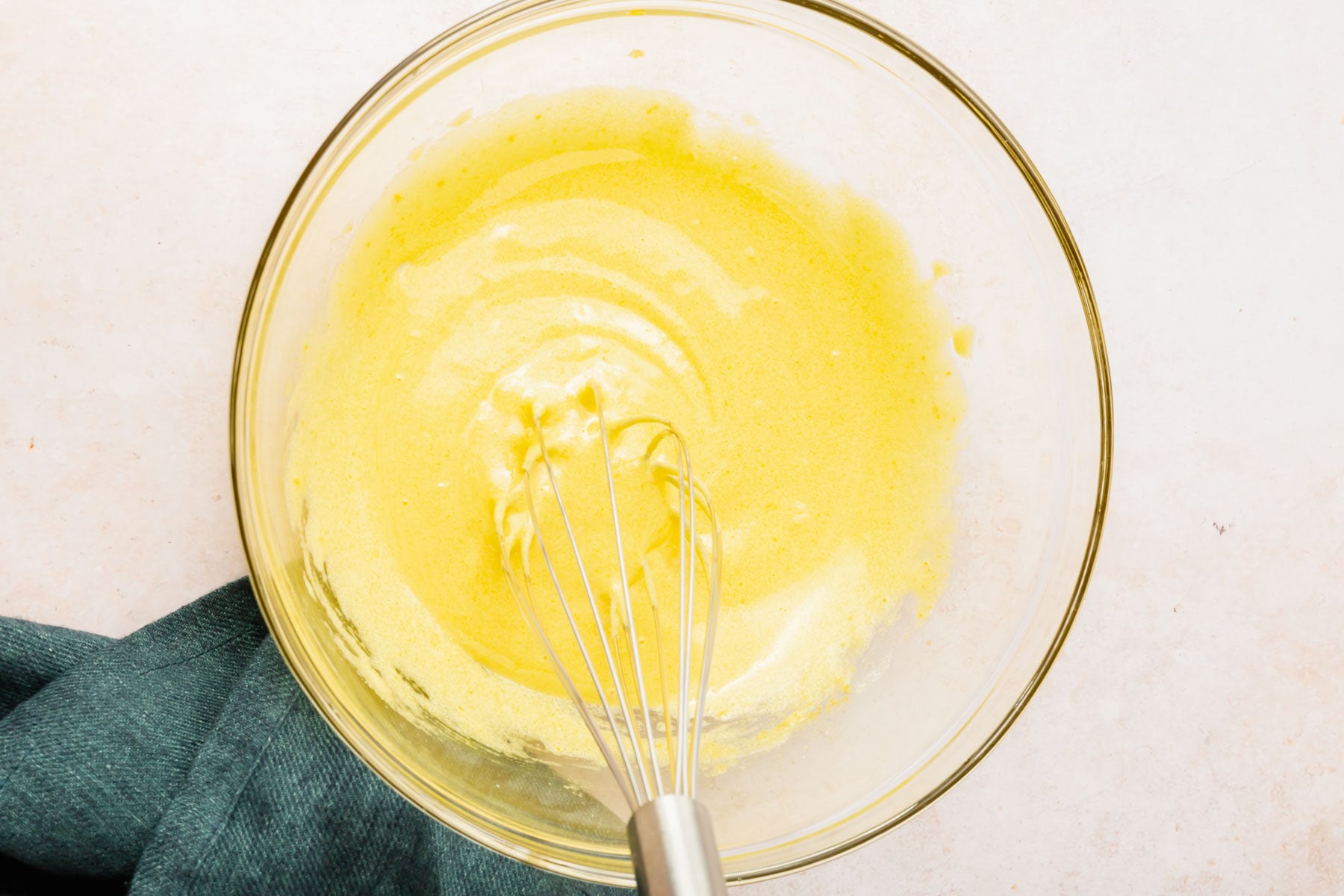 A whisk mixing together egg yolks and granulated sugar in a large glass bowl.
