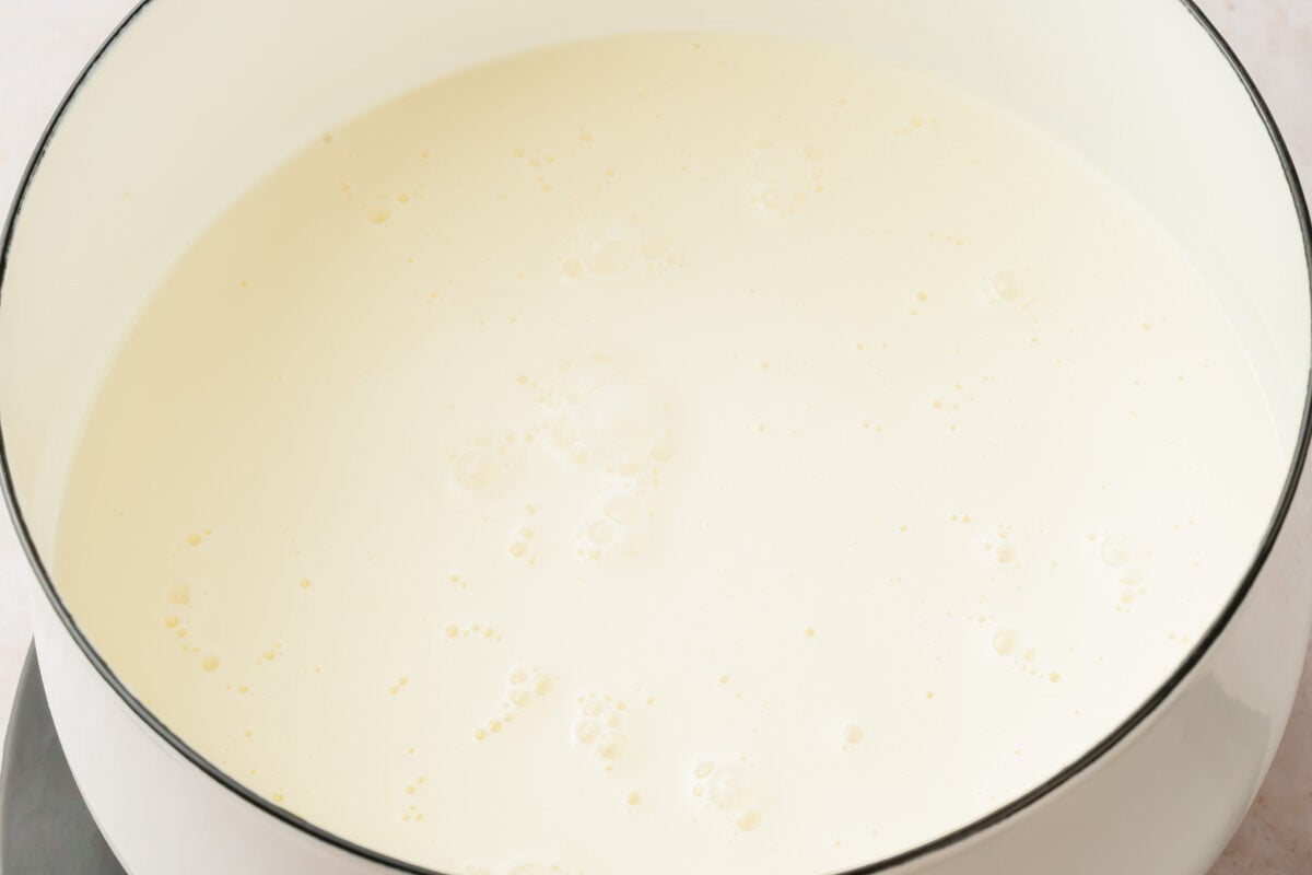 A white saucepan on a portable burner with heavy cream in it that is simmering.