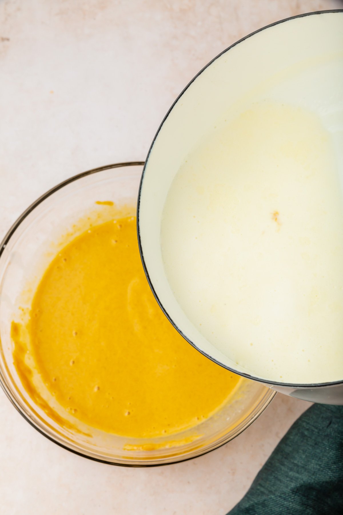Heavy cream being poured from a white saucepan into a pumpkin and egg yolk mixture to make creme brulee.