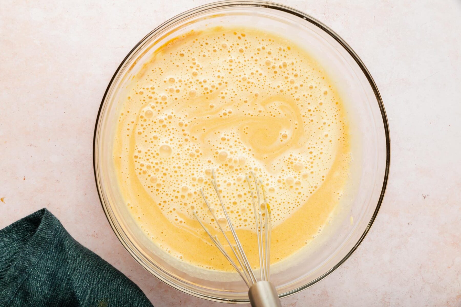 A glass mixing bowl with pumpkin crème brûlée mixture with a wire whisk.