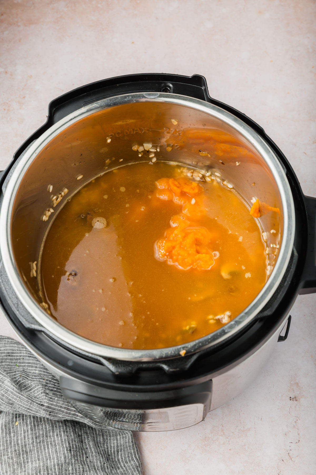 An Instant Pot filled with chicken broth, arborio rice, and pumpkin puree before mixing together.