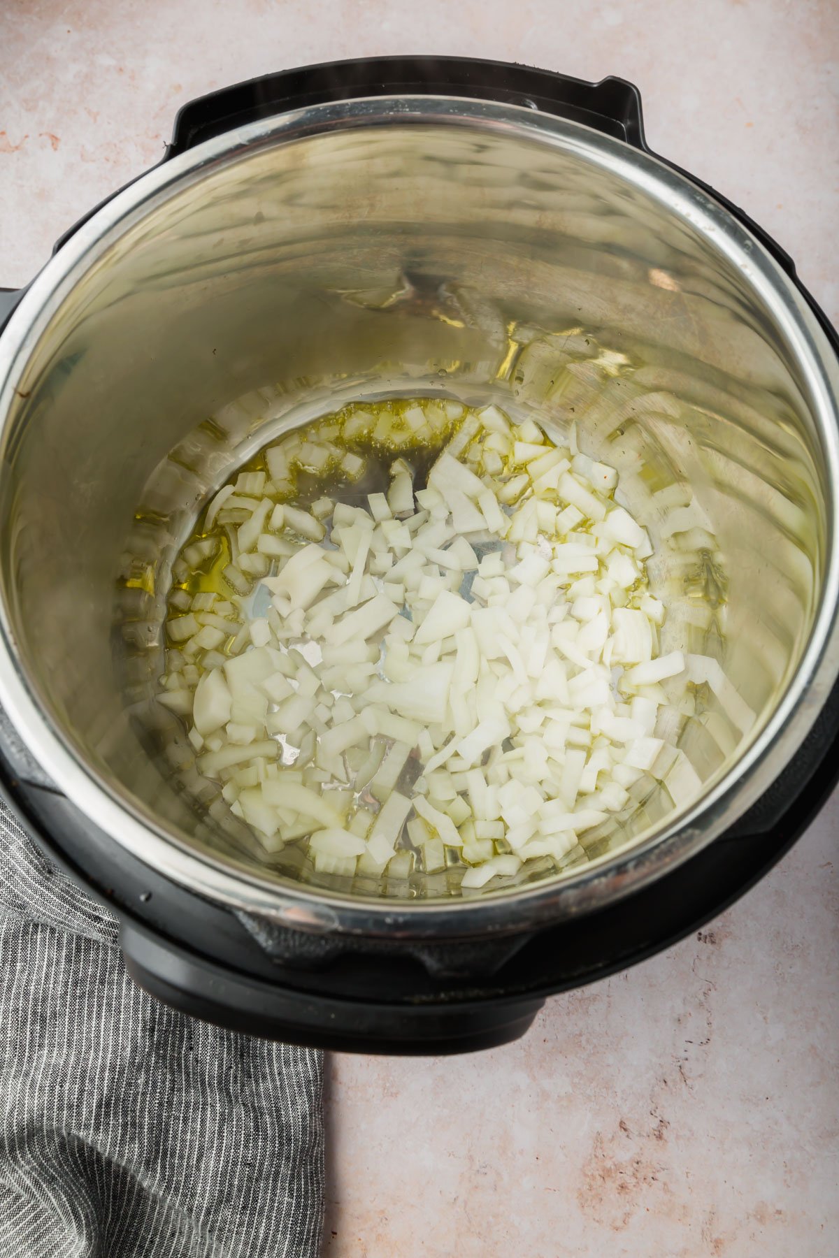 An Instant pot with diced white onions cooking in olive oil.