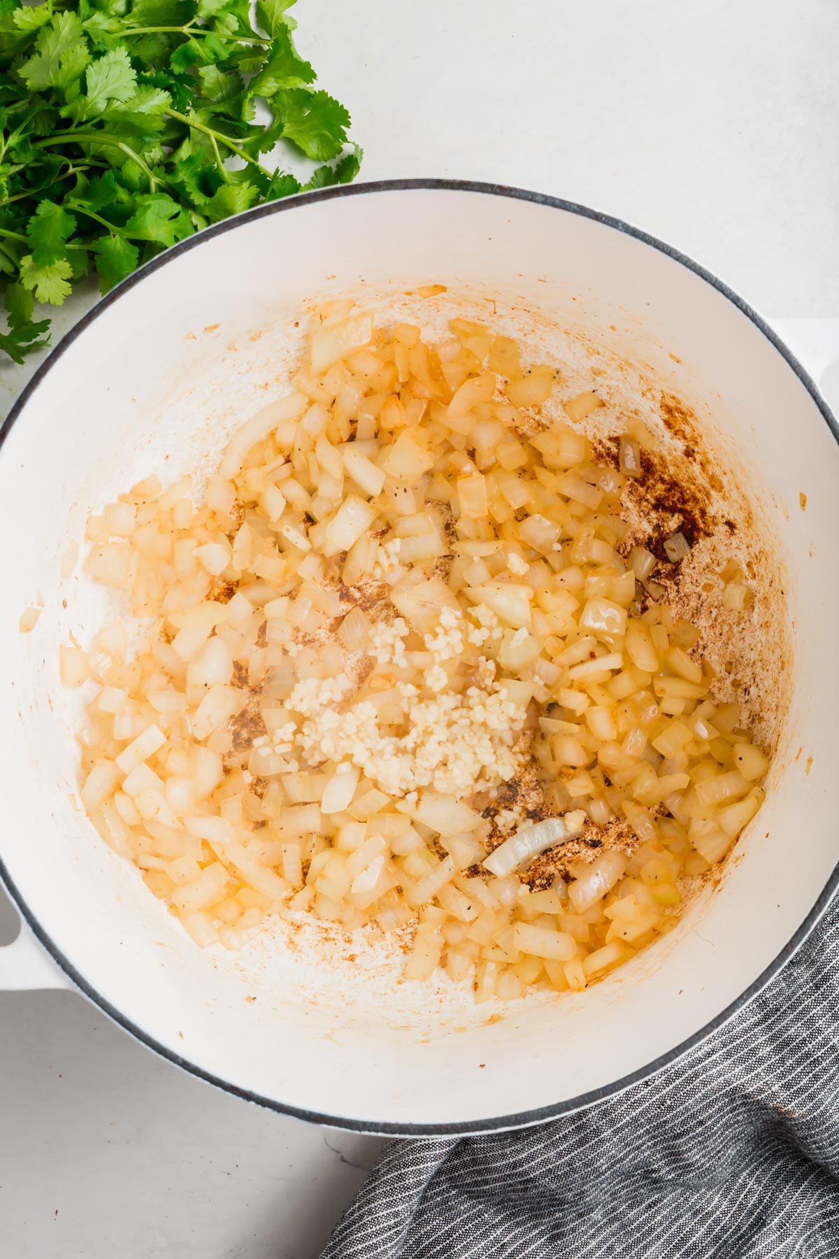 An overhead view of a dutch oven with sautéed onion and minced garlic.