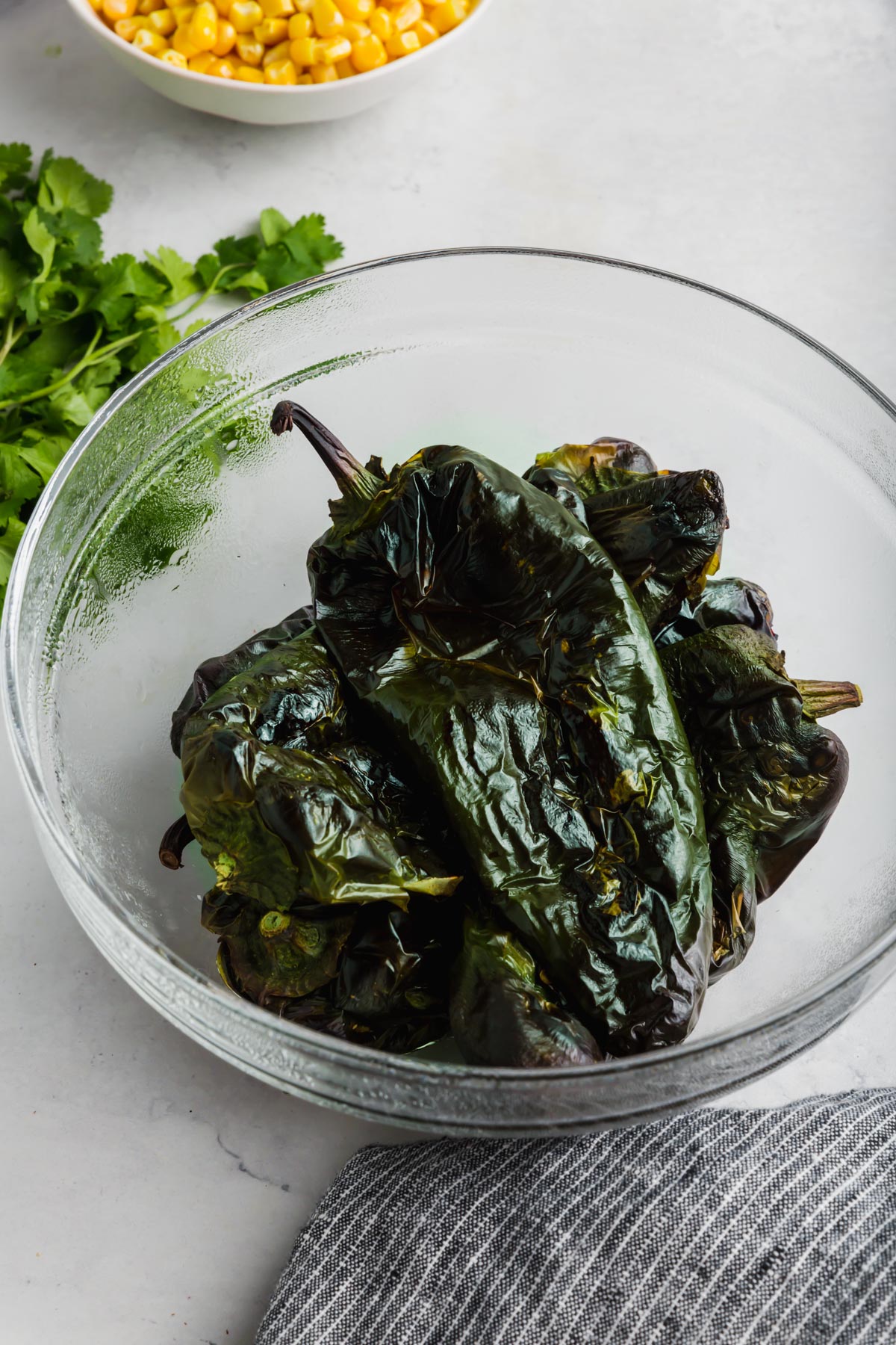 A bowl of roasted poblano peppers with a bowl of corn in the background.