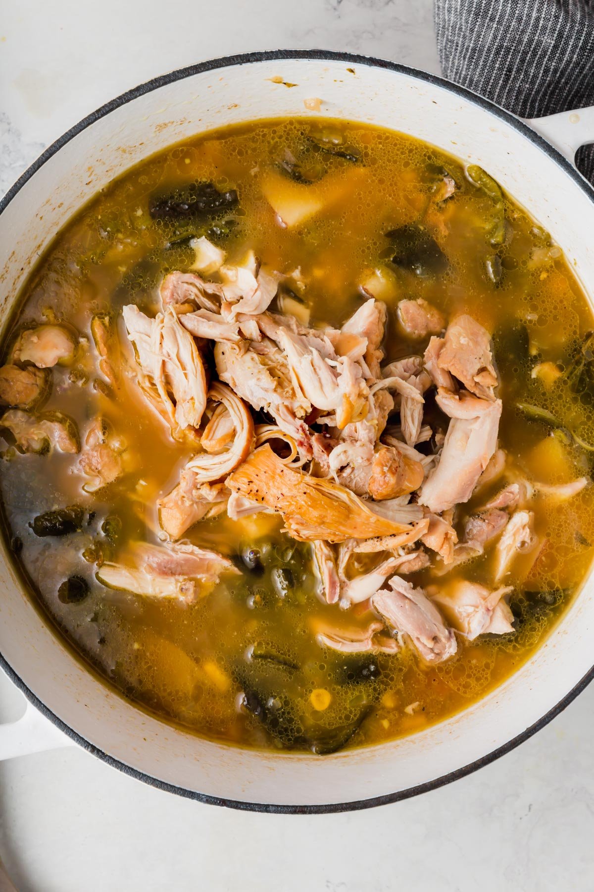 A white dutch oven with a poblano soup topped with shredded chicken.