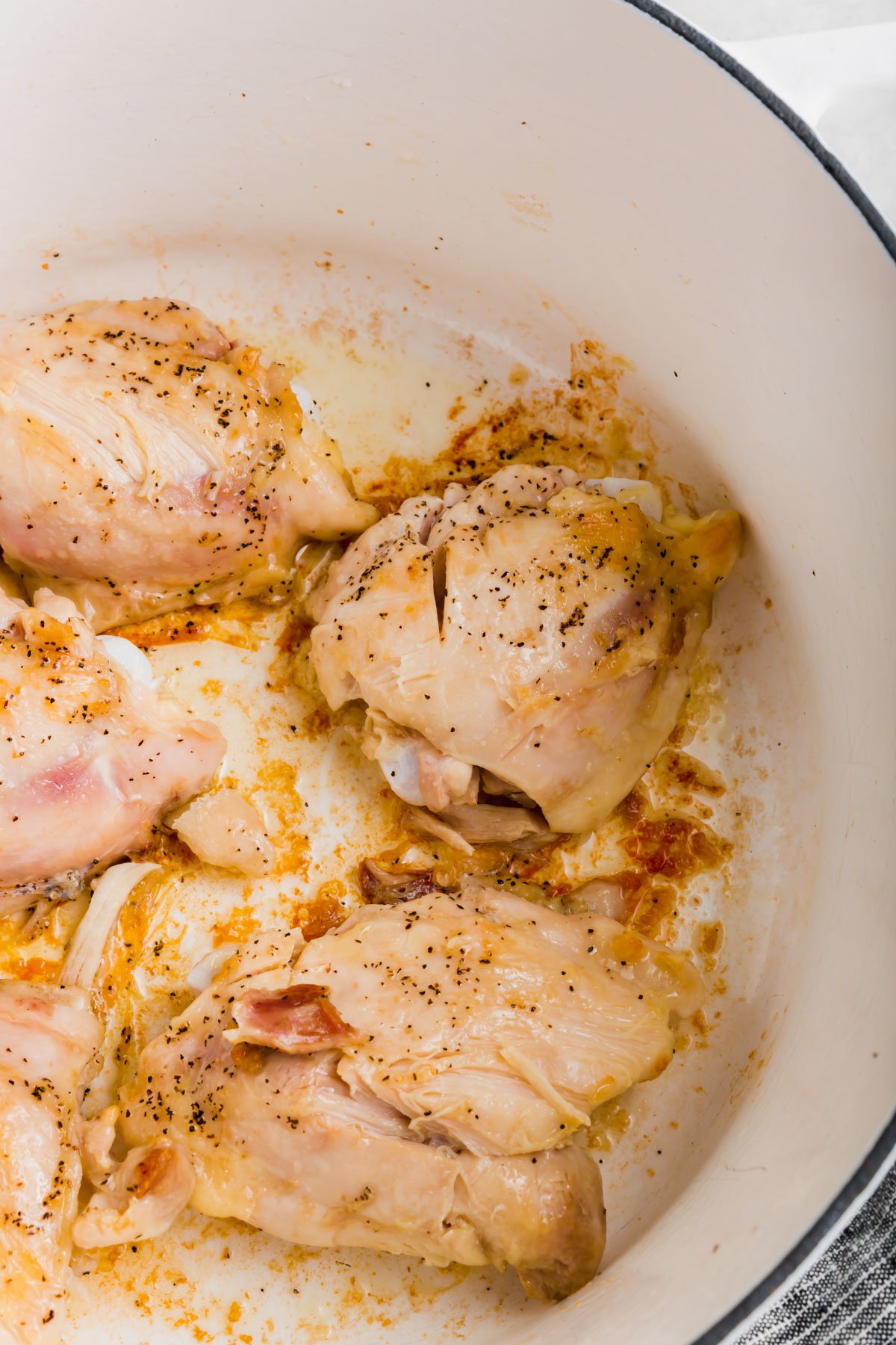 A close up of chicken thighs cooking in a white dutch oven.