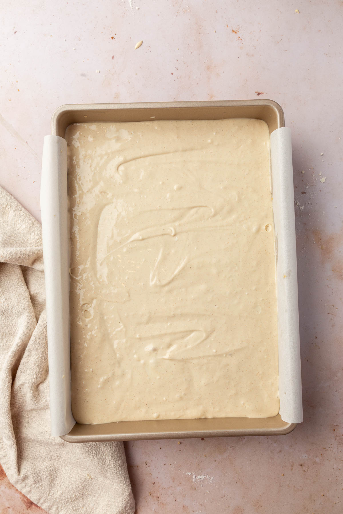 A metal rectangular baking pan lined with parchment paper and filled with a cheesecake batter before baking in the oven.