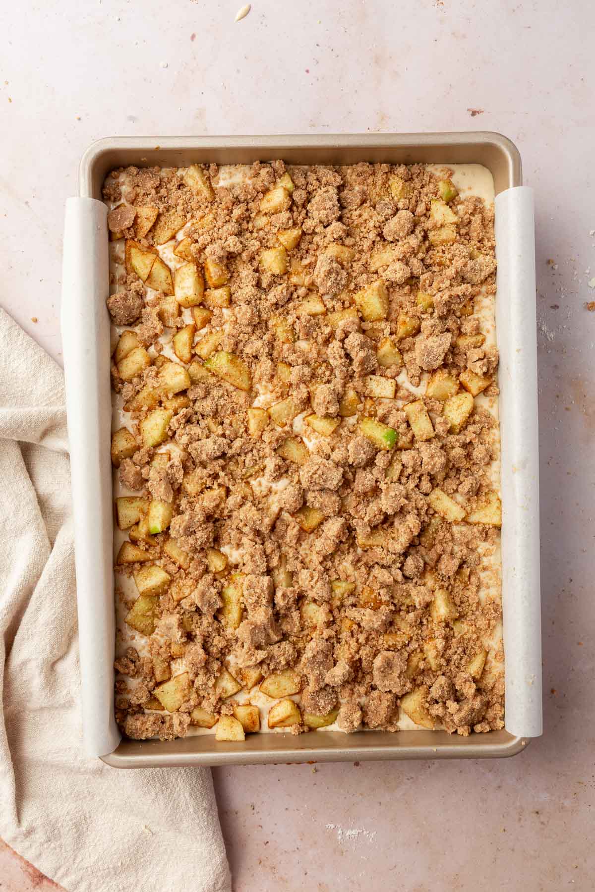 A rectangular baking pan filled with a cheesecake filled topping with spiced granny smith apple cubes and gluten-free cinnamon streusel before baking in the oven.