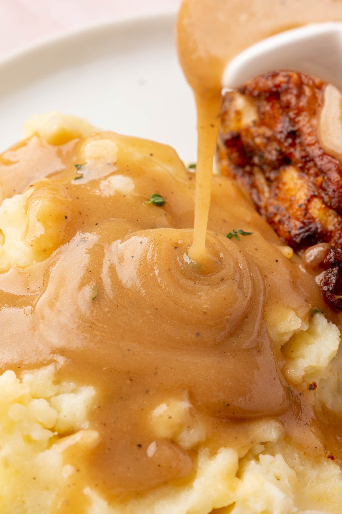 Gluten-free gravy being poured over a serving of mashed potatoes.