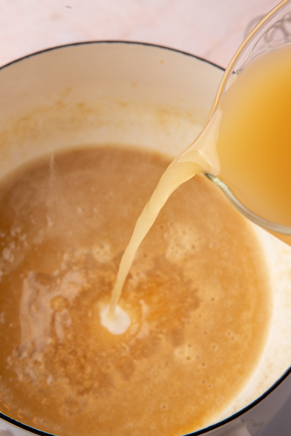 Turkey stock being poured into a saucepan with a gluten-free roux.