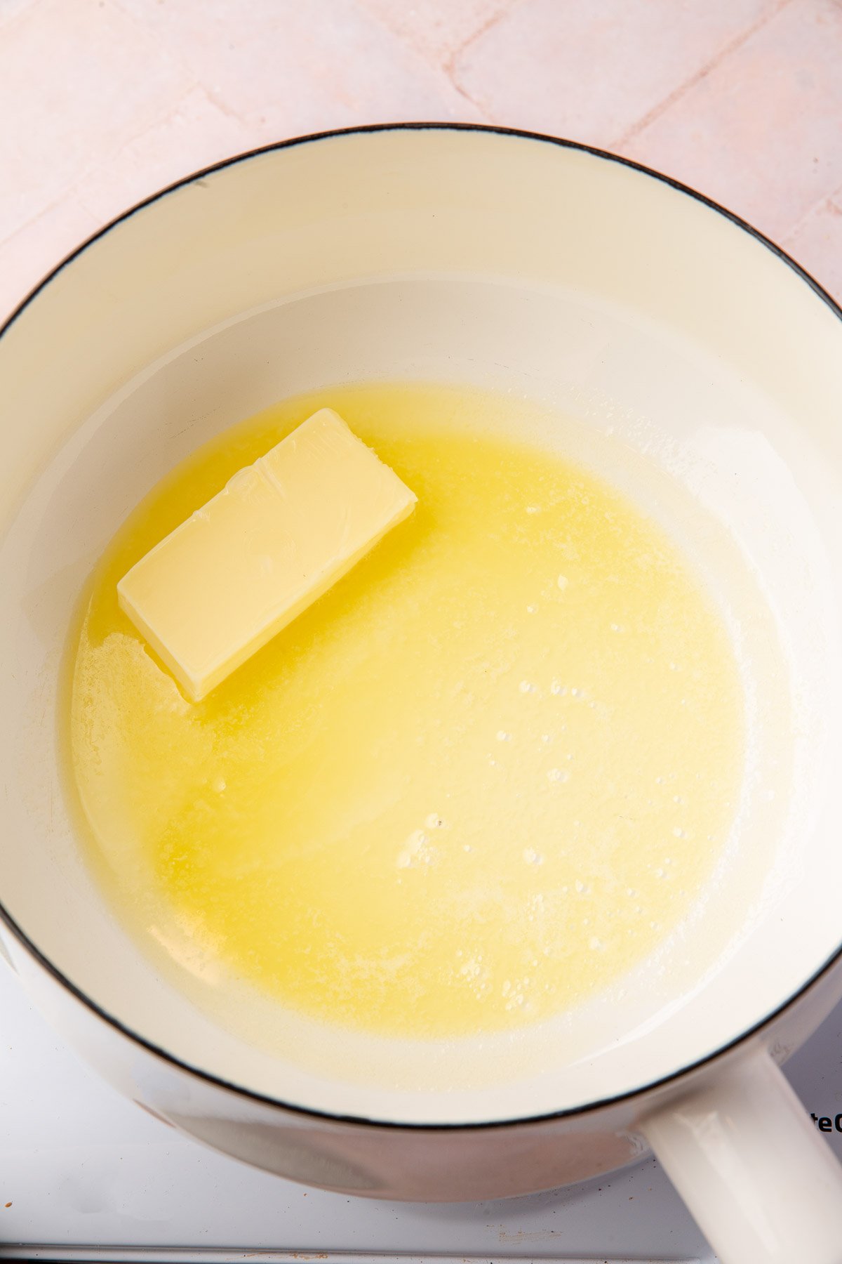 A stick of butter melting in a white saucepan.