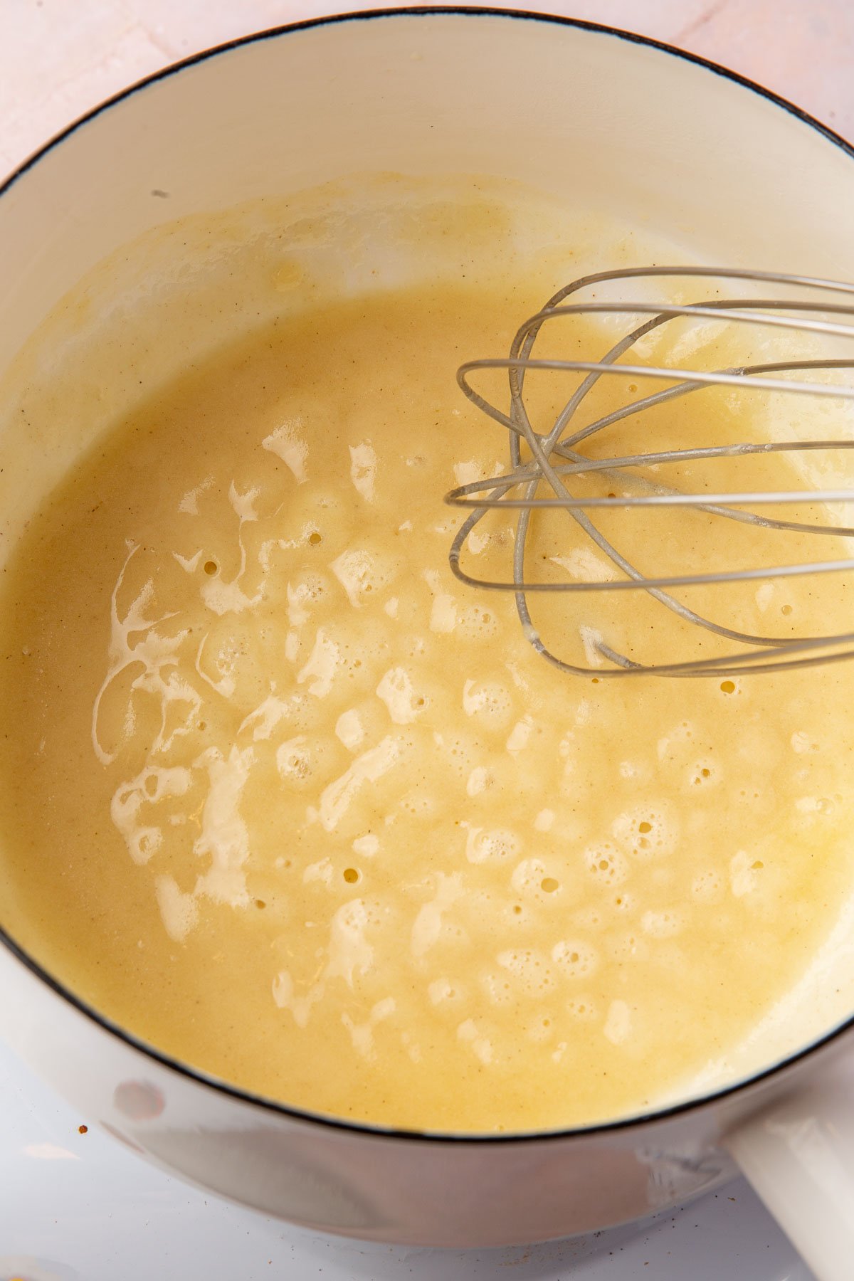 A blonde gluten-free roux being stirred by a wire whisk in a saucepan.