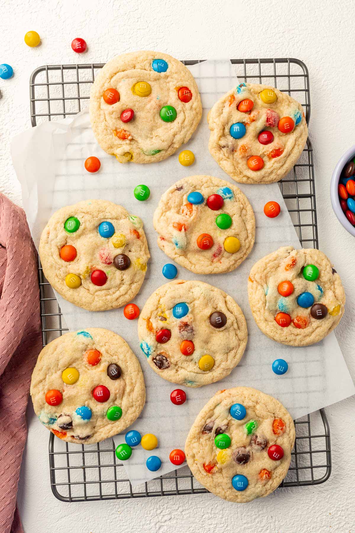 Eight gluten-free M&M sugar cookies on a wire cooling rack lined with parchment paper with stray M&Ms on the surface.