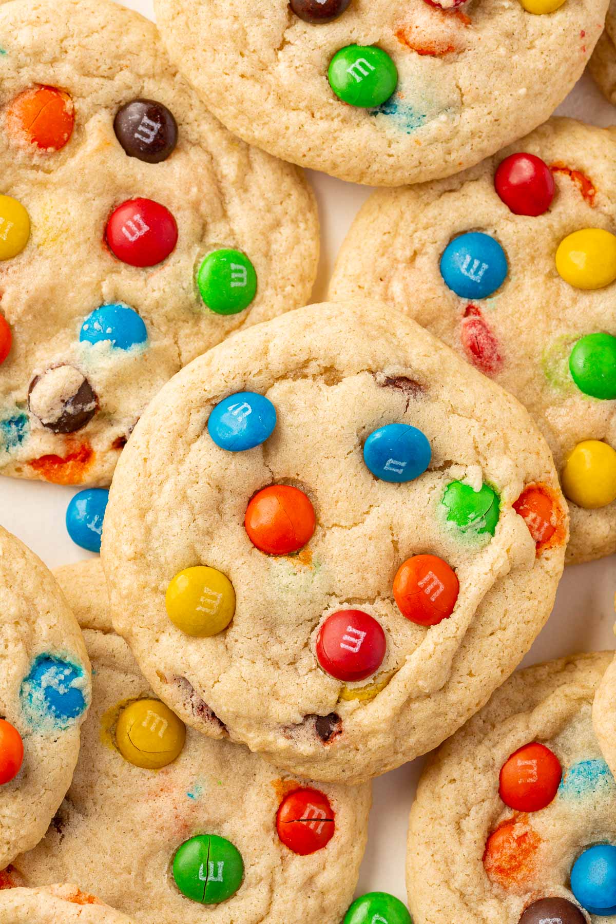 Gluten free M&M sugar cookies overlapping one another on a piece of parchment paper.