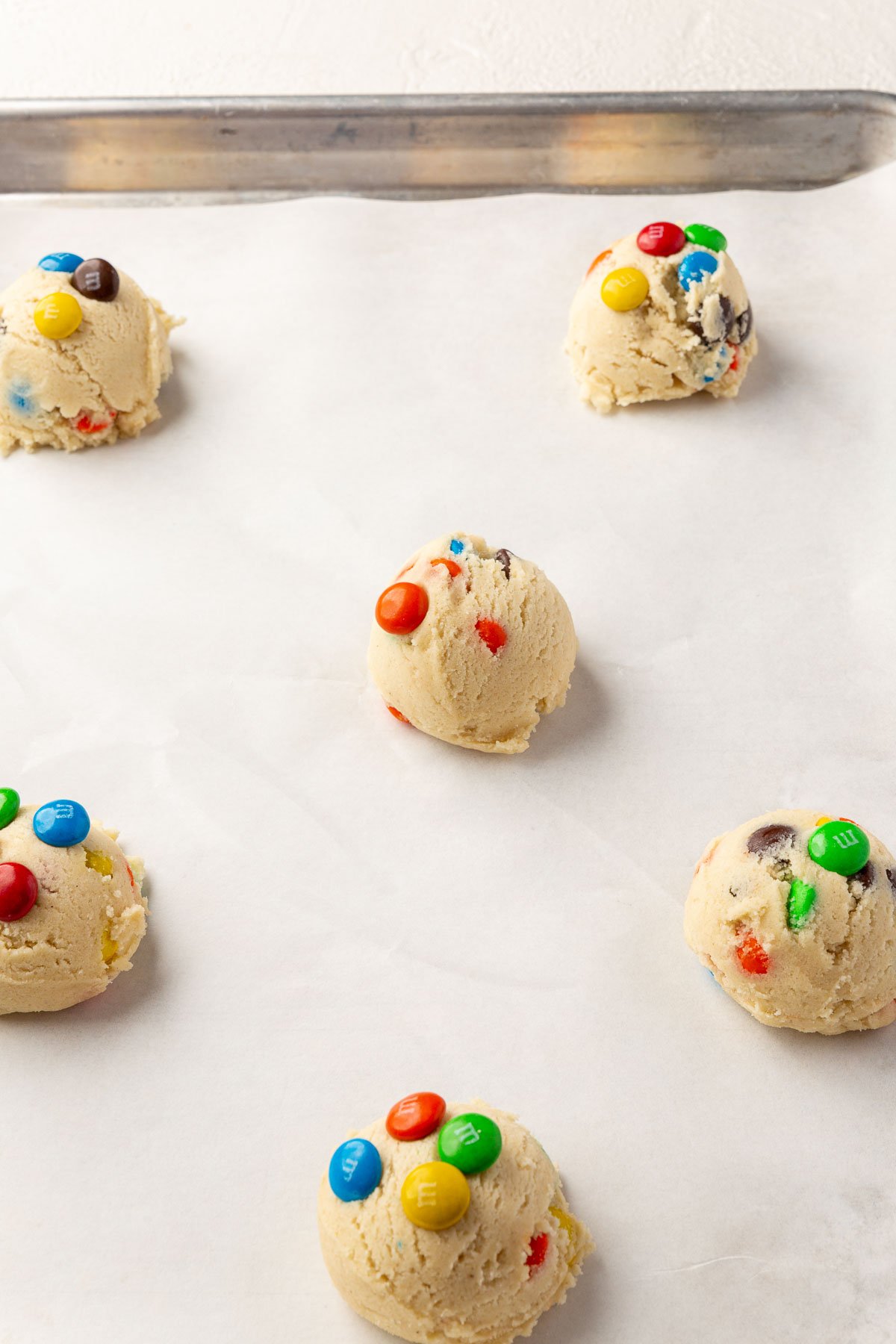 Balls of gluten free M&M cookie dough on a baking sheet lined with parchment paper before baking in the oven.