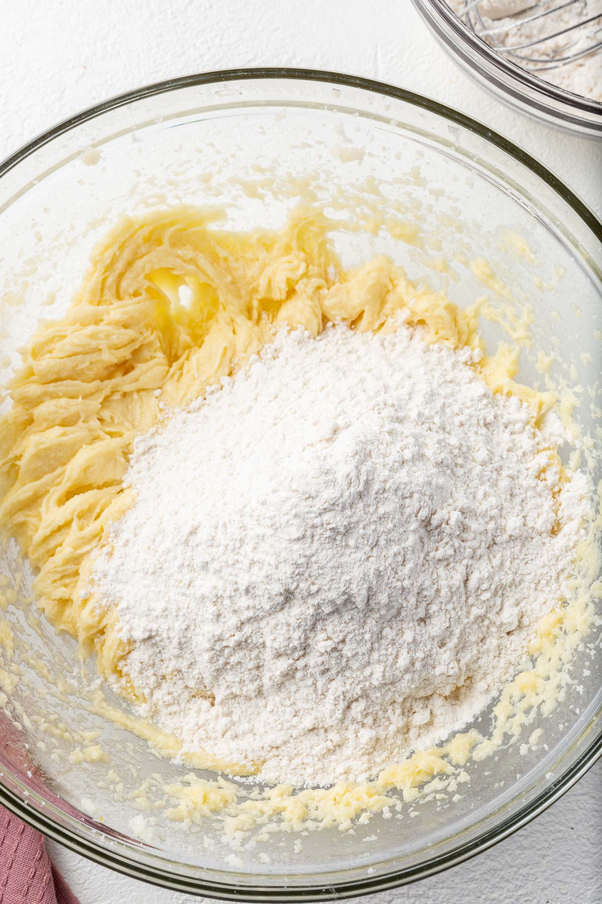 A glass mixing bowl with creamed butter and sugar in it topped with a gluten-free flour mixture.