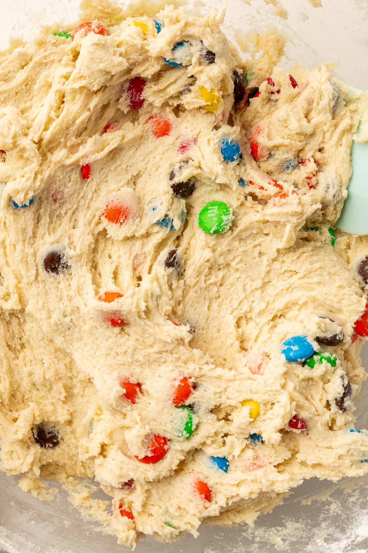 A close up of gluten-free M&M sugar cookie dough in a glass mixing bowl.