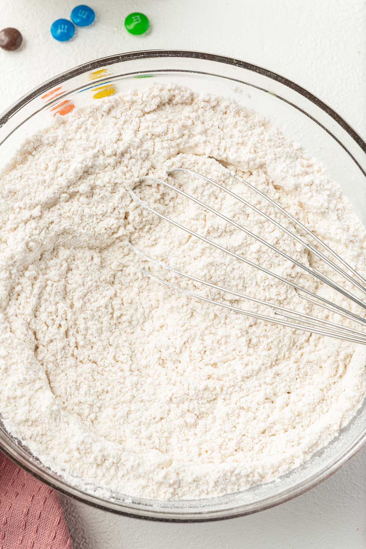 A close up of a glass mixing bowl with a gluten-free flour blend whisked together with a wire whisk.