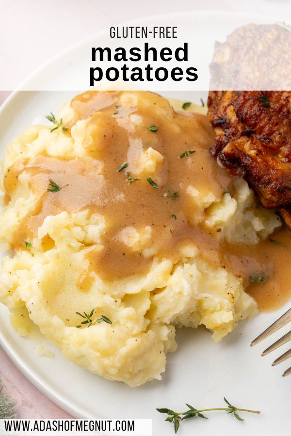 A serving of mashed potatoes topped with gluten-free gravy and crispy chicken thigh in the background.