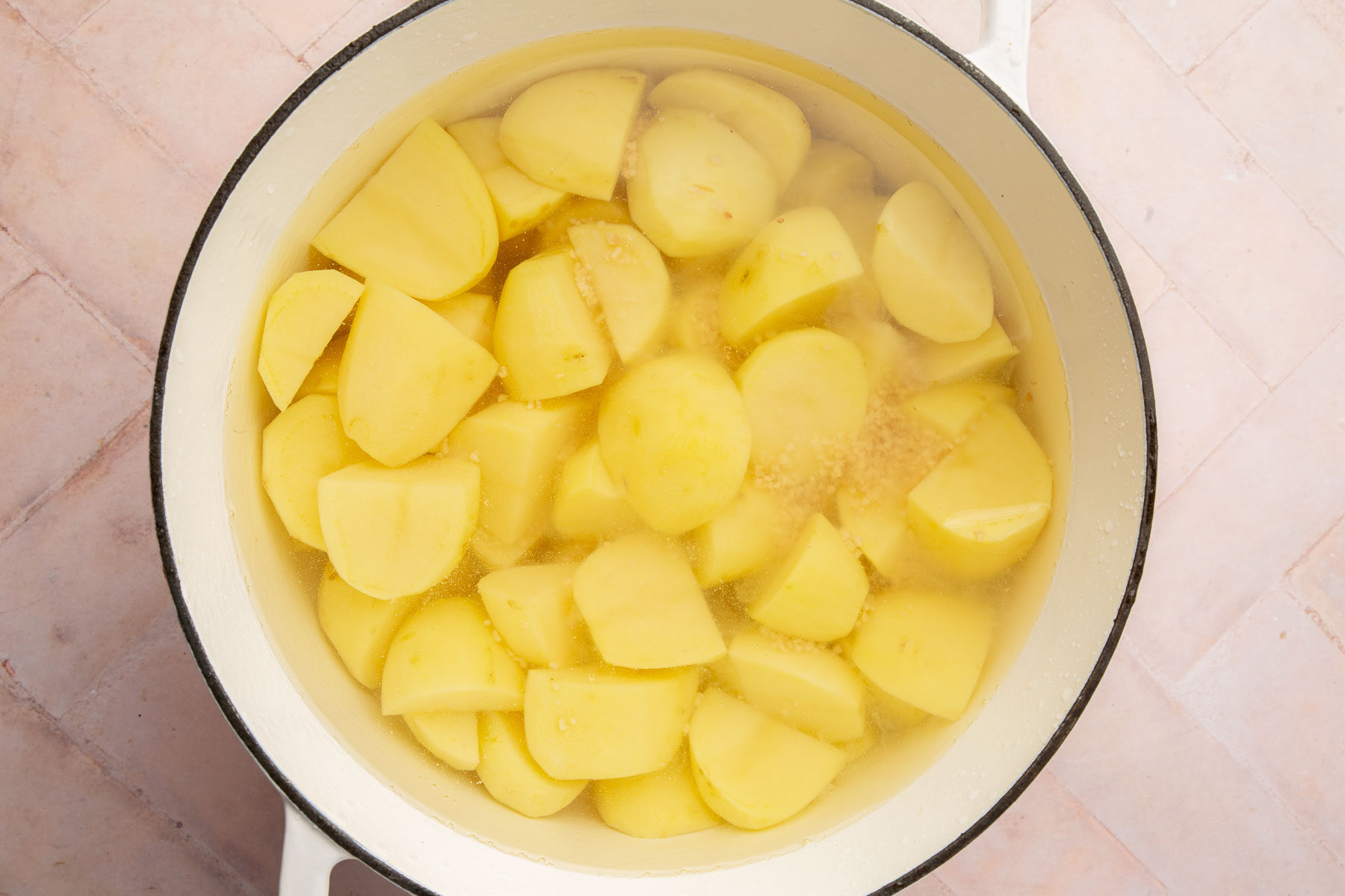 A dutch oven with potato quarters and minced garlic in water ready to boil.