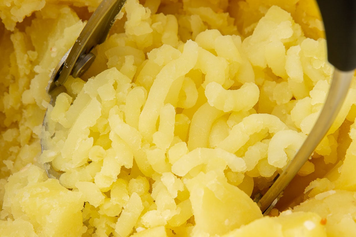 A potato masher mashing yukon gold potatoes in a dutch oven.