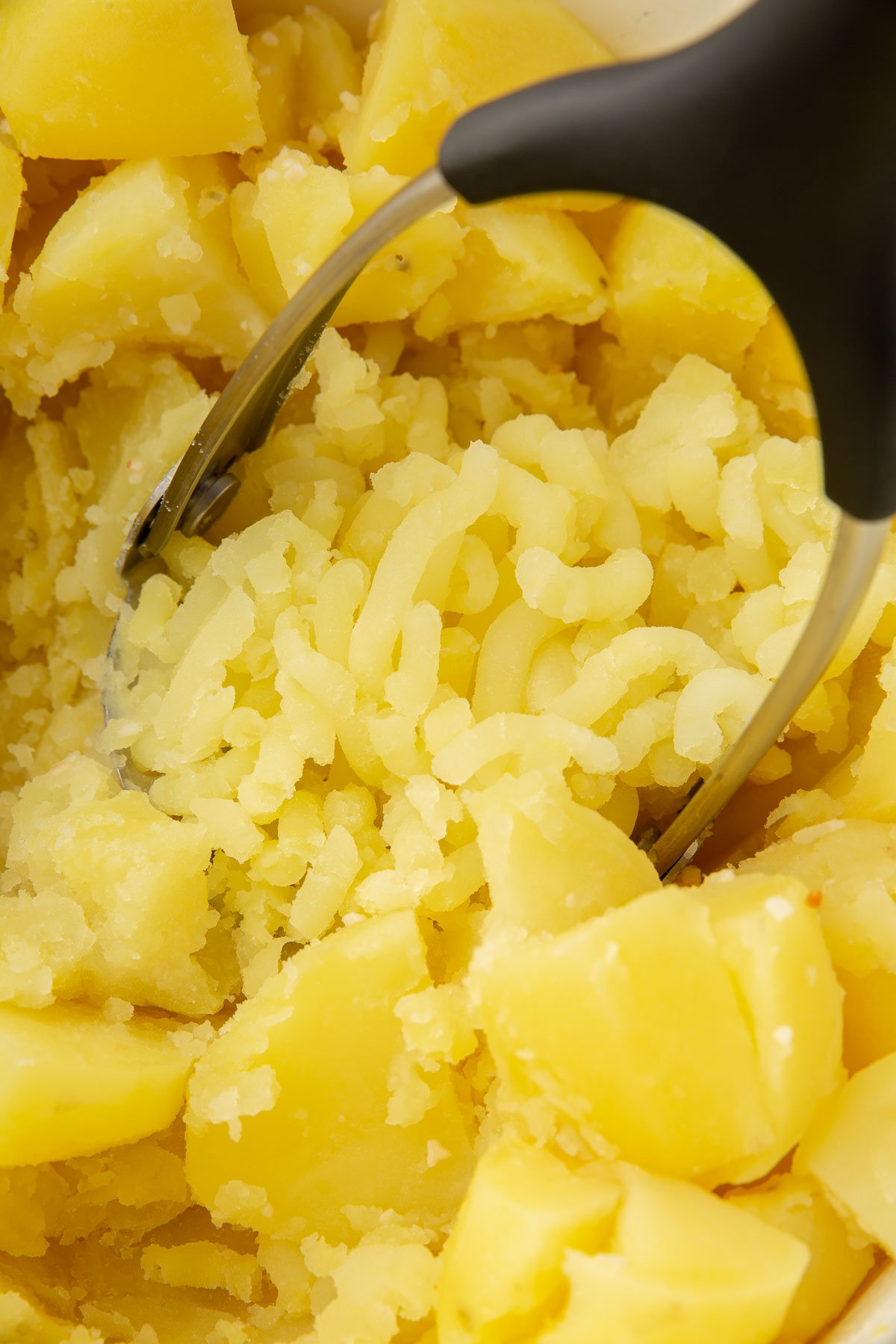 A potato masher mashing yukon gold potatoes in a dutch oven.