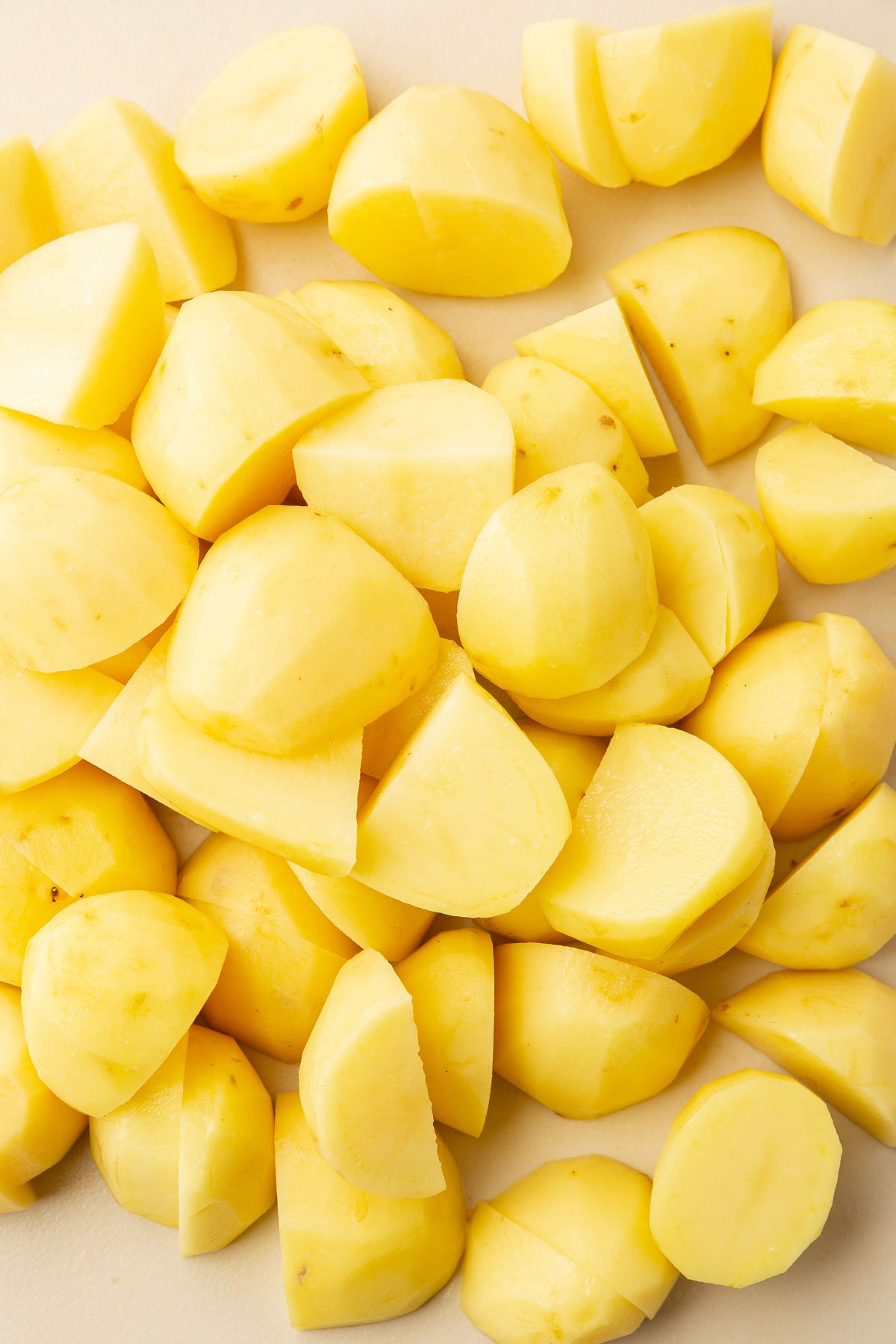 A close up of peeled yukon gold potato quarters on a cutting board.