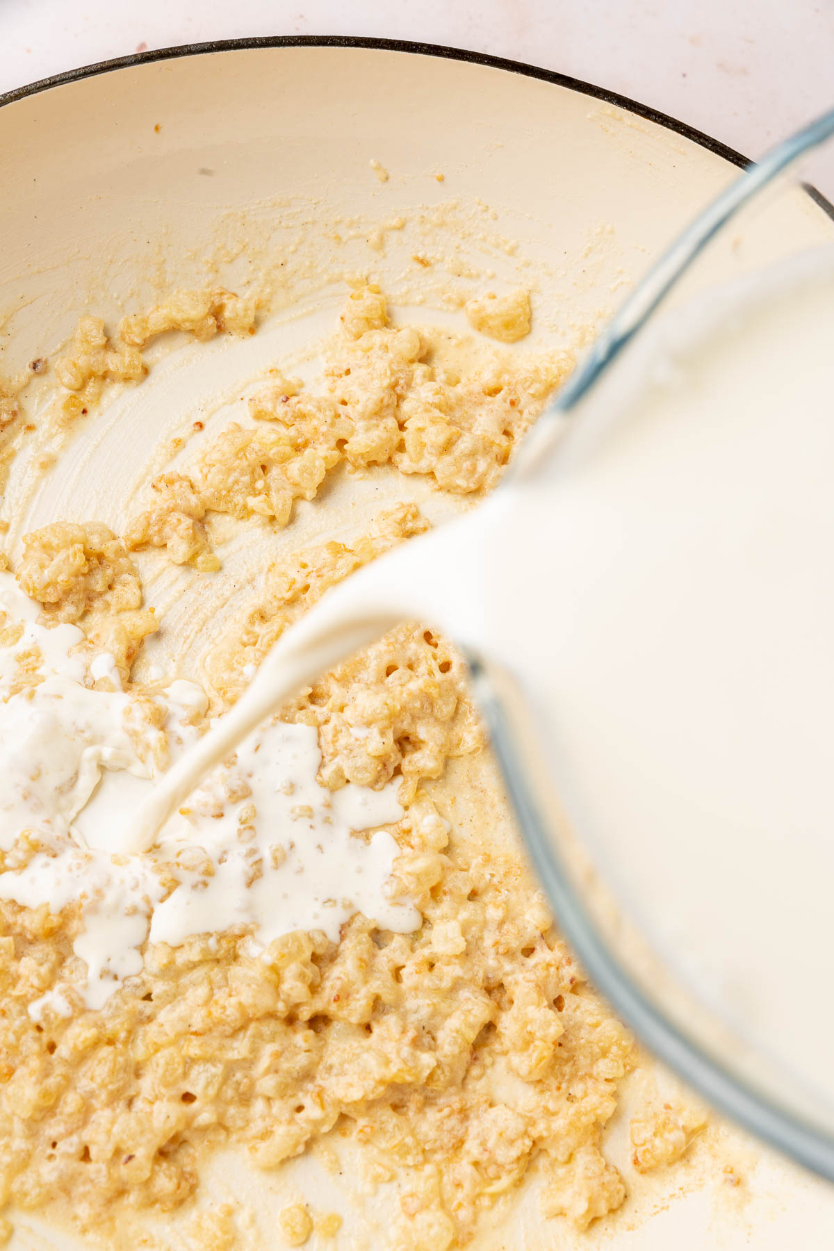 A glass measuring cup pouring heavy cream into a gluten-free roux.