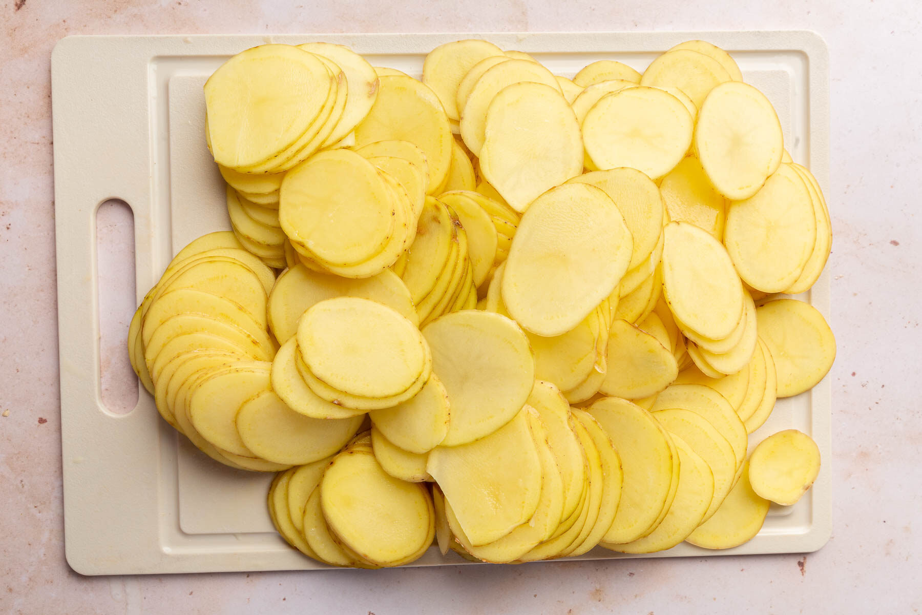 Slices of yukon gold potatoes on a cutting board.