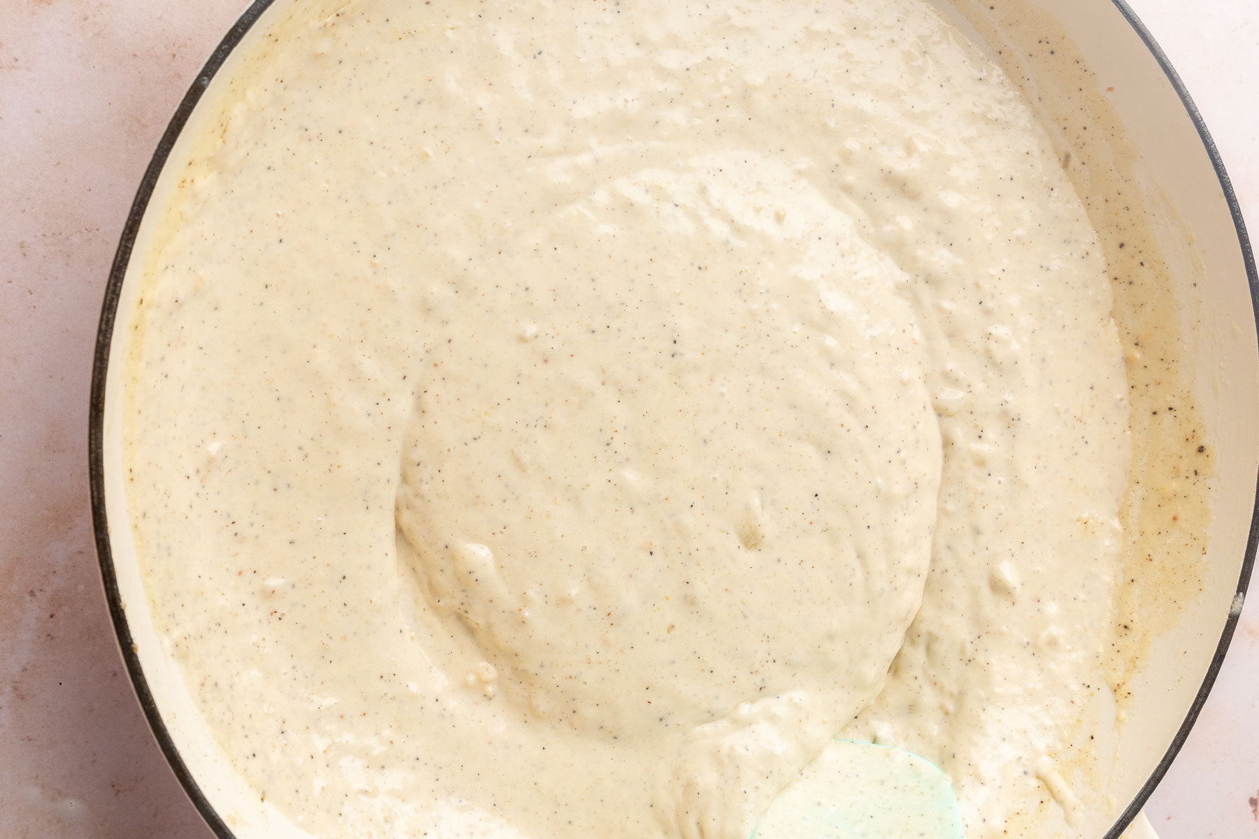 A braising pan with a gluten-free cream sauce with black pepper in it.