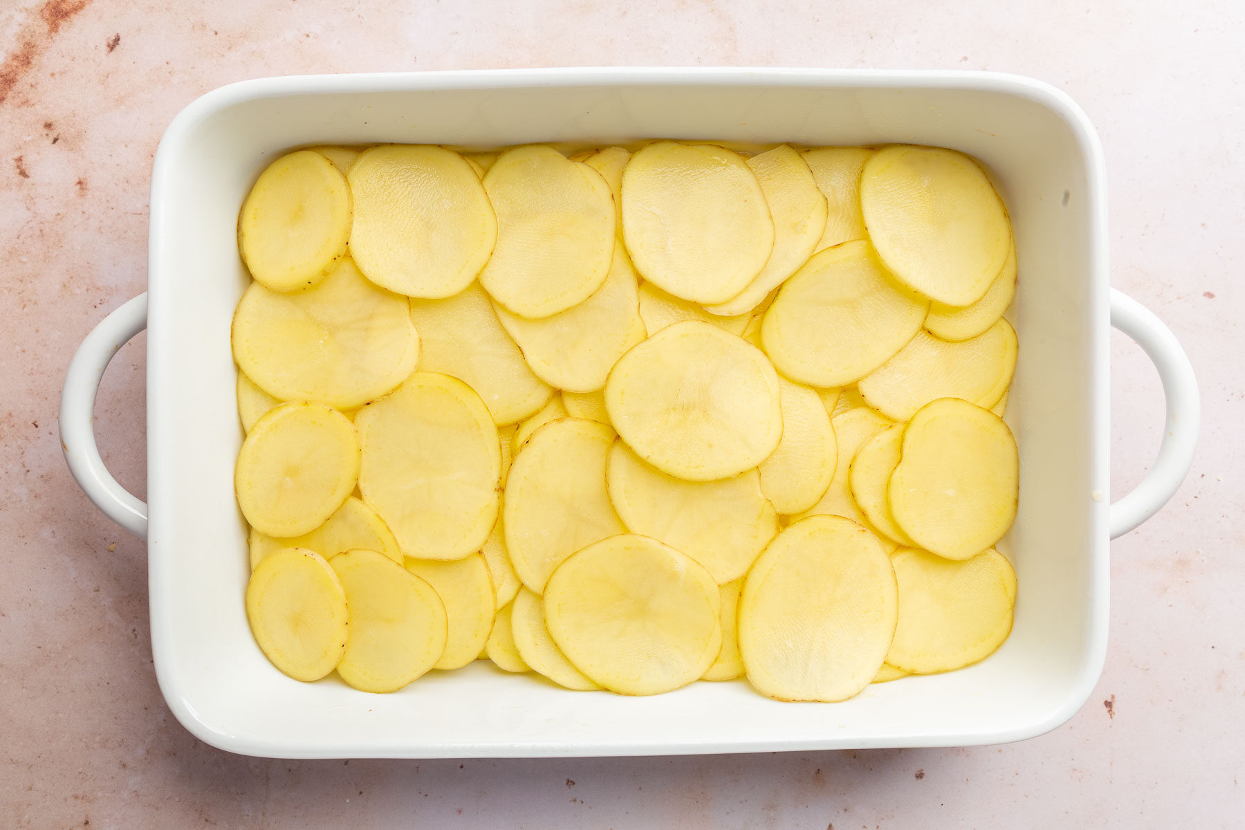 A rectangle baking pan with thinly sliced potatoes in it that are slightly overlapping.