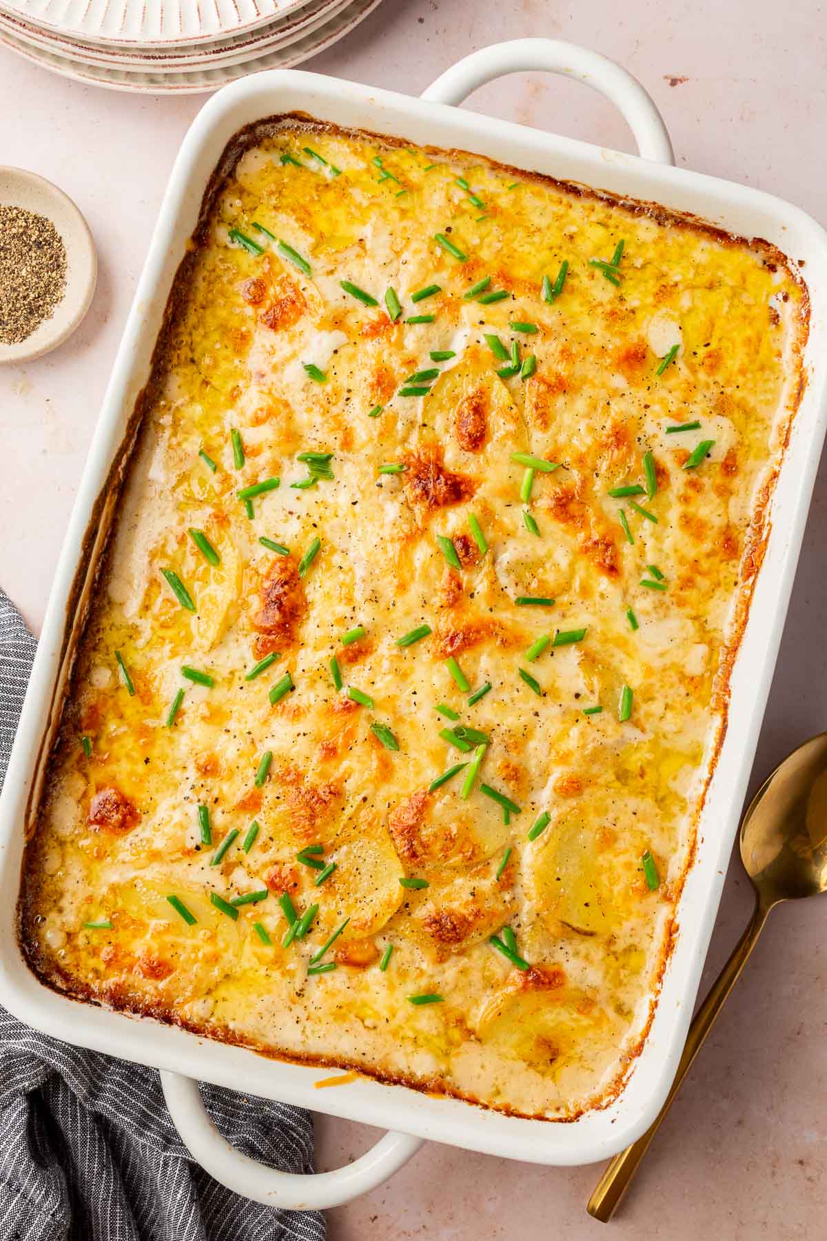 A white rectangle baking dish with baked gluten-free scalloped potatoes from the oven with freshly chopped chives on top.